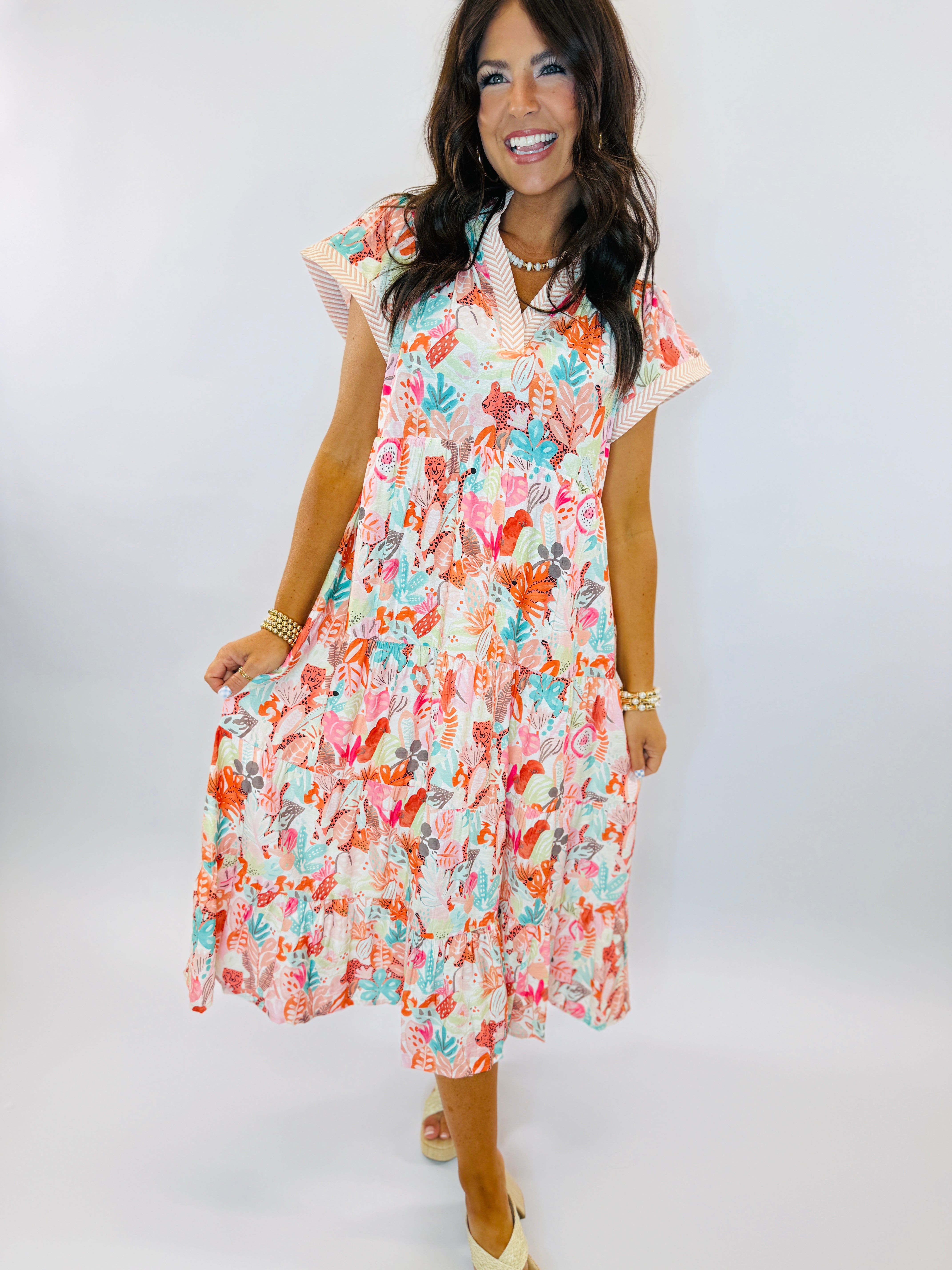 Woman wearing a colorful floral print midi dress with ruffled sleeves and tiered skirt in vibrant coral, turquoise, and pink.