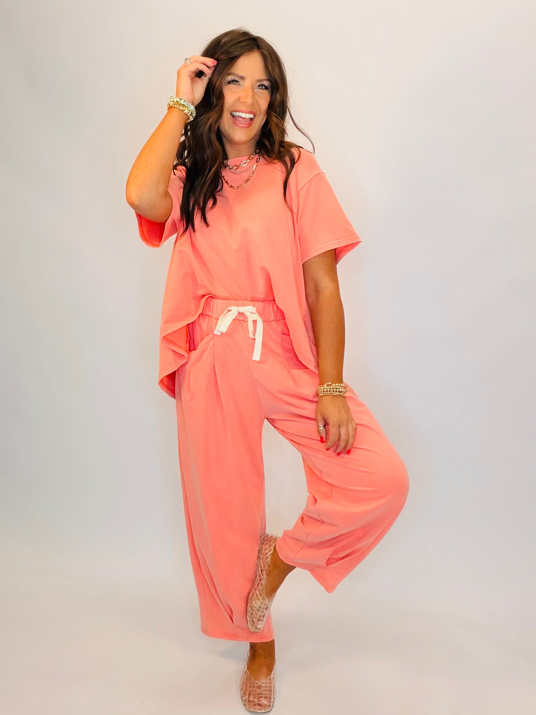 Woman wearing coral pink matching set with oversized top and drawstring pants, styled with gold jewelry and heels.