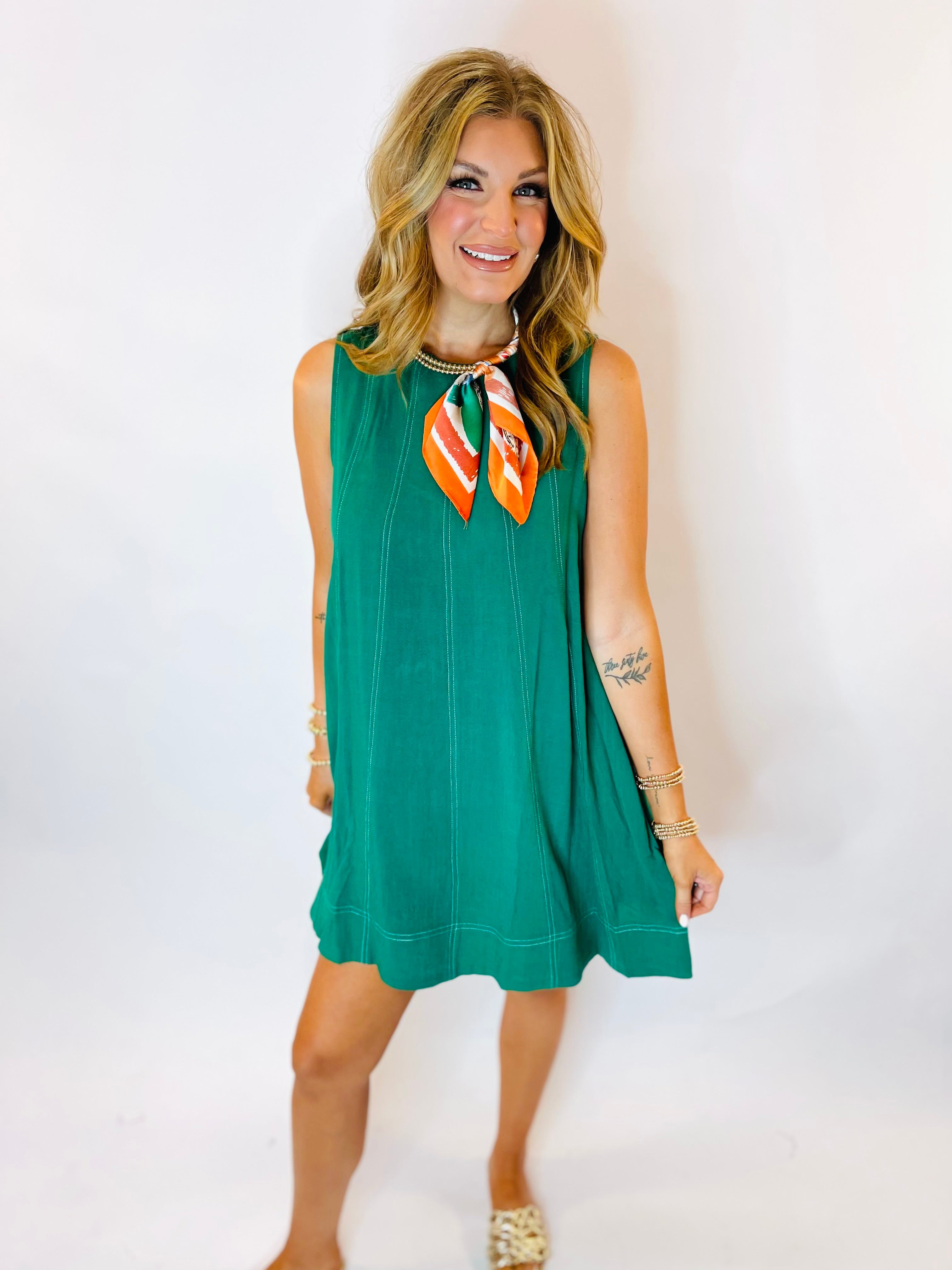 Kira sleeveless green swing mini dress with contrast stitching, styled with orange striped neck scarf.