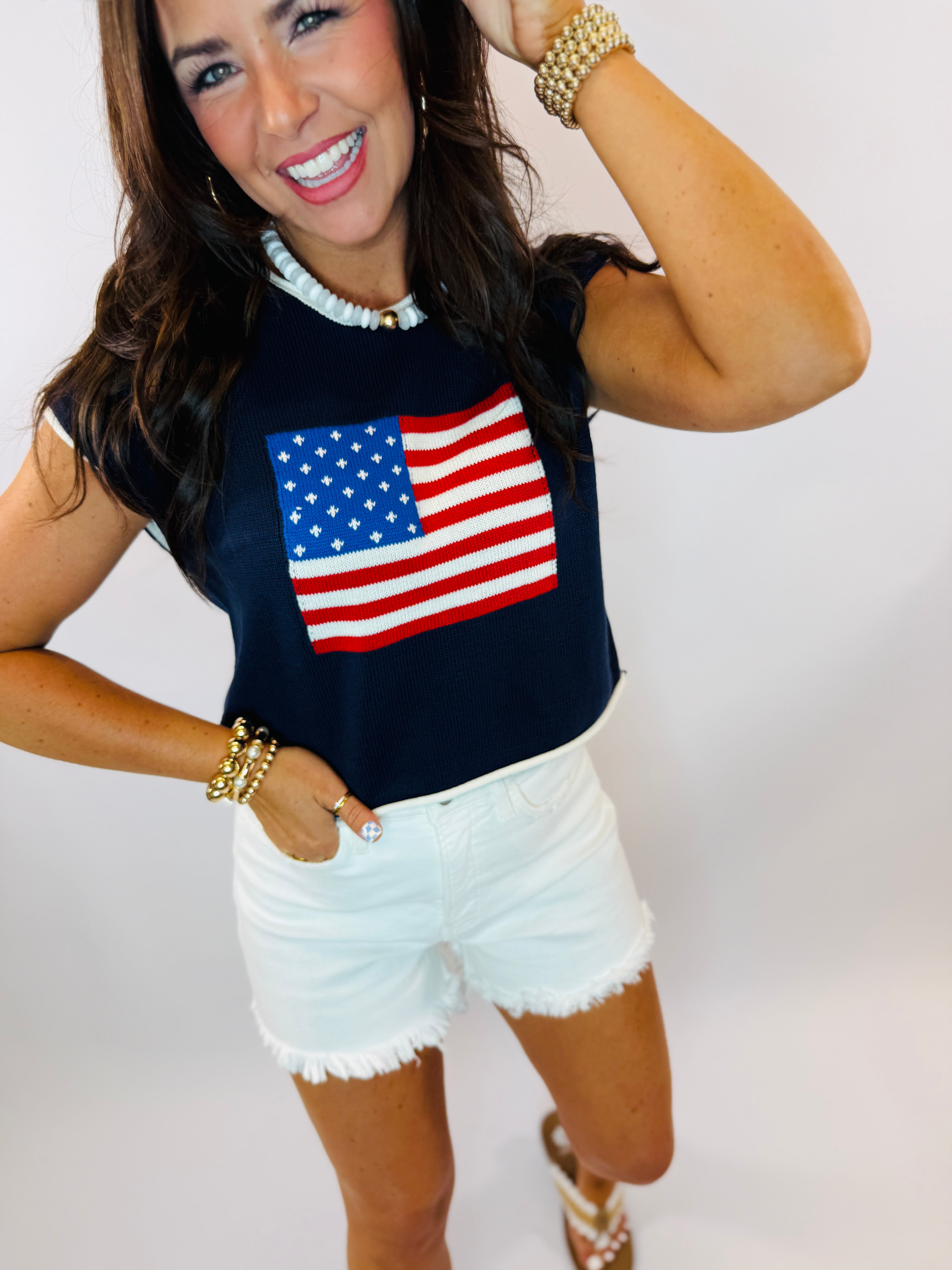 Navy blue sleeveless sweater top with knitted American flag design, worn with white denim shorts.