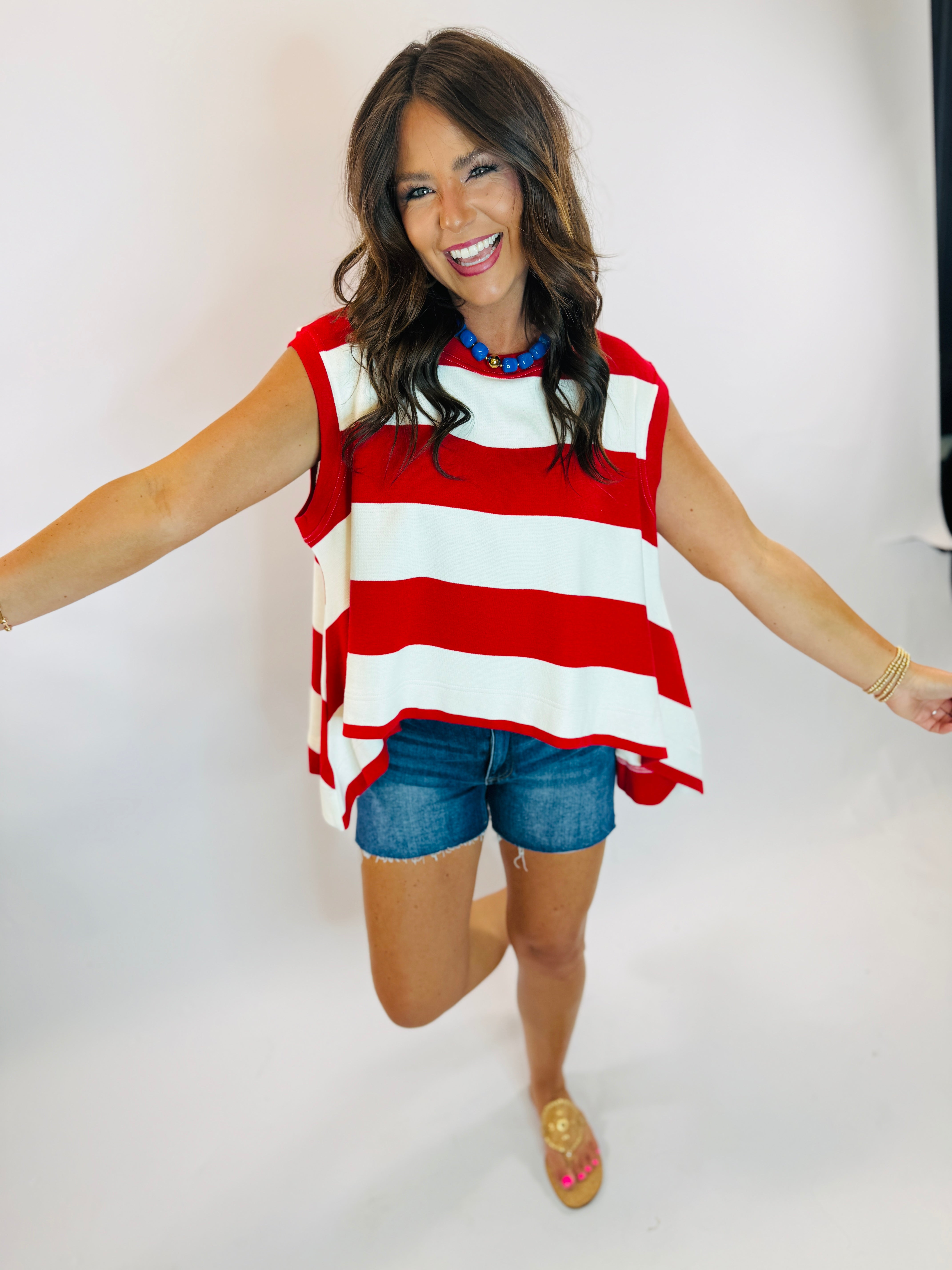 Kennedy Top sweatshirt in red and white wide stripes, sleeveless style, worn with denim shorts.