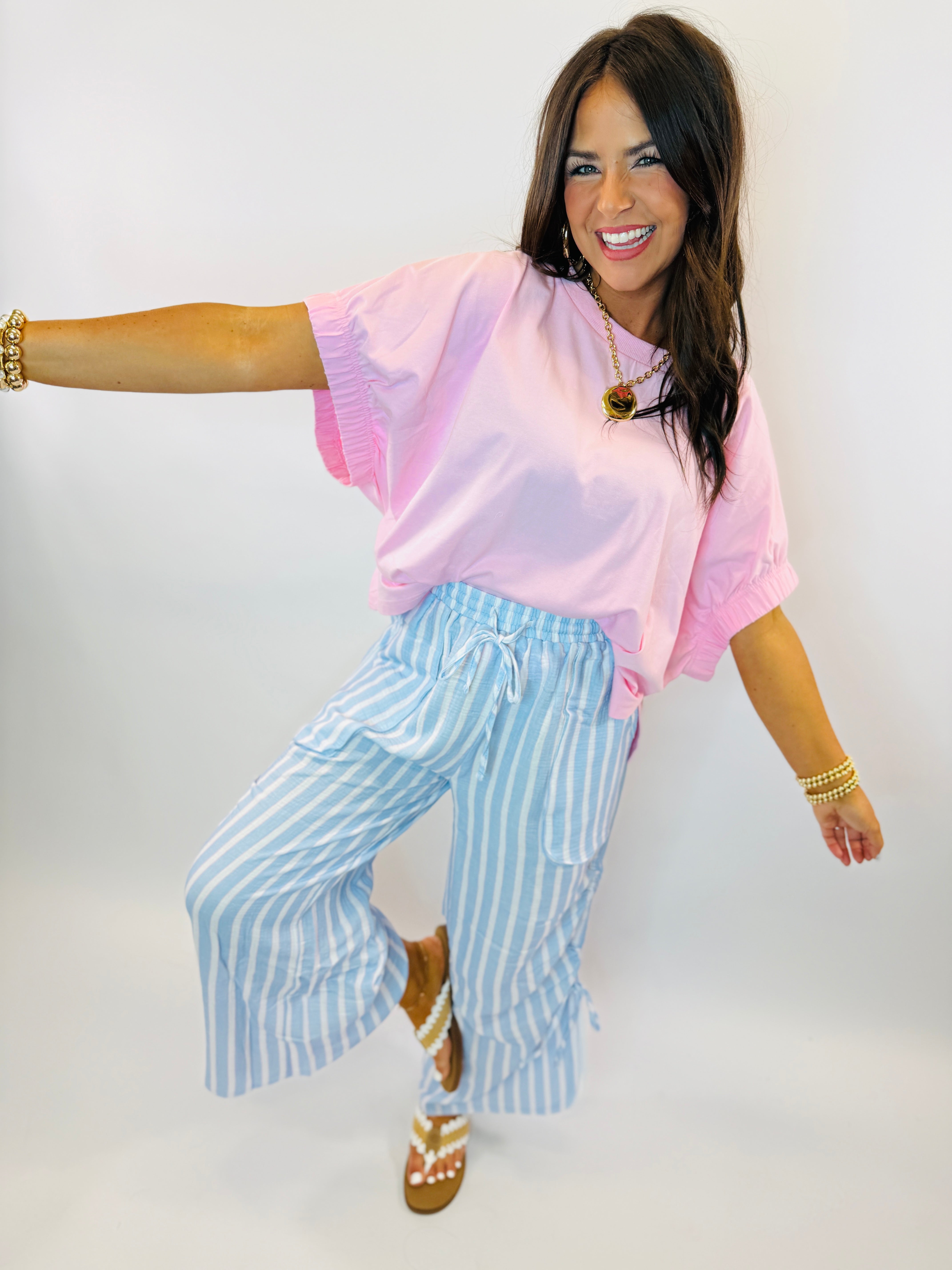 Woman wearing pink tie-dye oversized top with ruffle sleeves, paired with blue and white striped pants.
