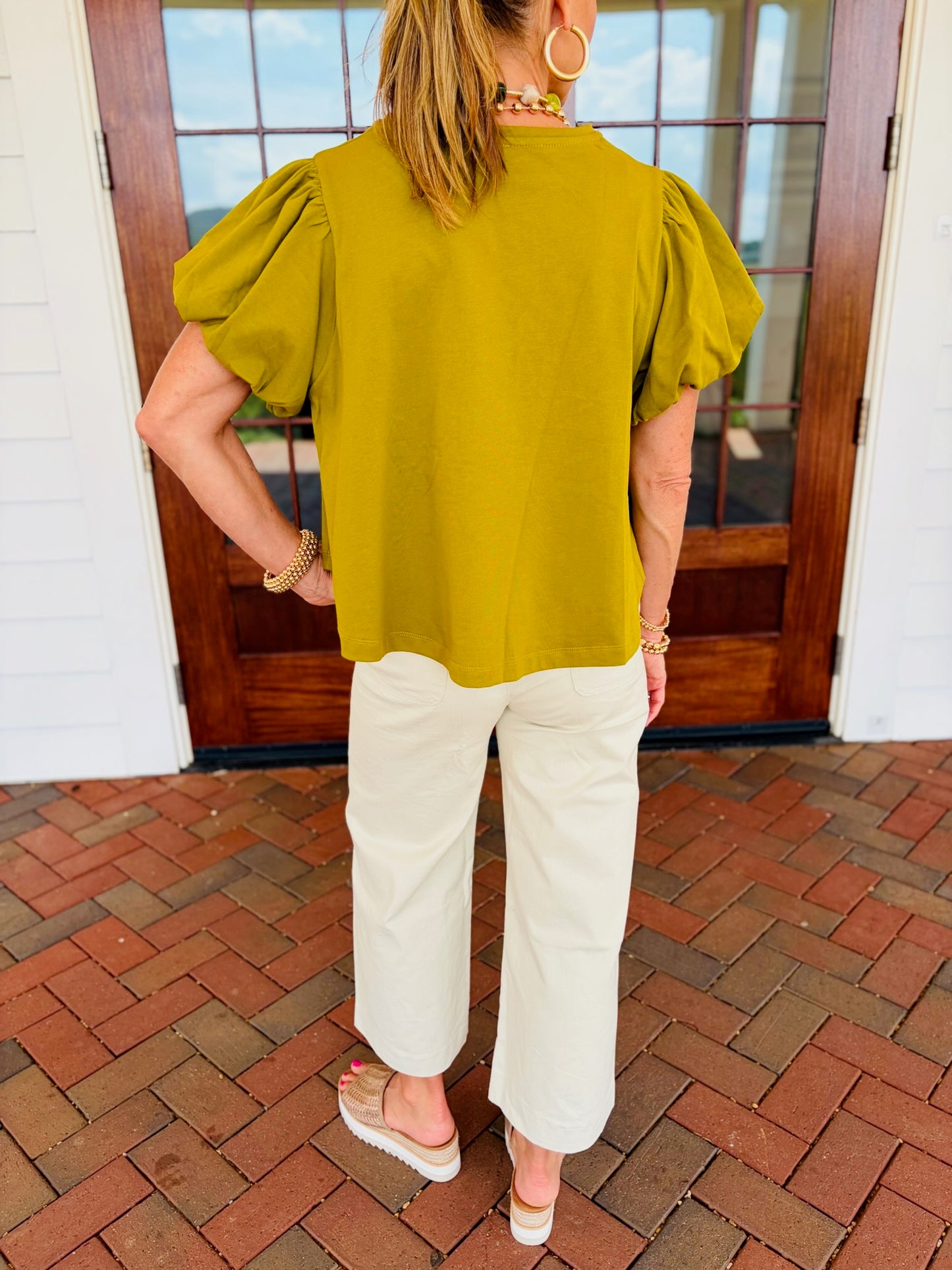 Back view of the Brittany martini olive cotton top, showing gathered puff sleeves and a straight hem, styled with cream cropped pants.