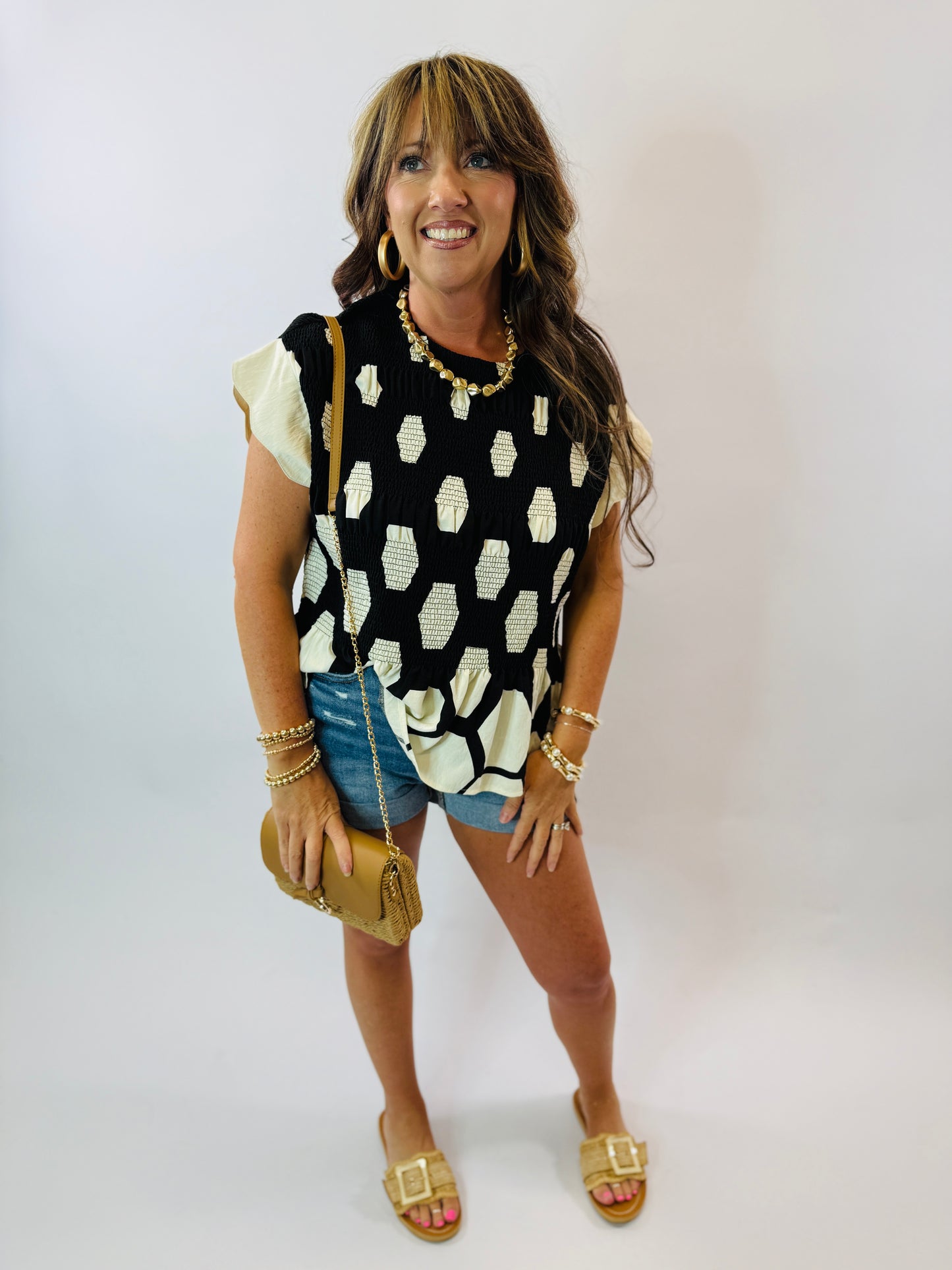 Woman wearing black and white polka dot Caroline top with ruffle sleeves, paired with denim shorts and gold accessories.