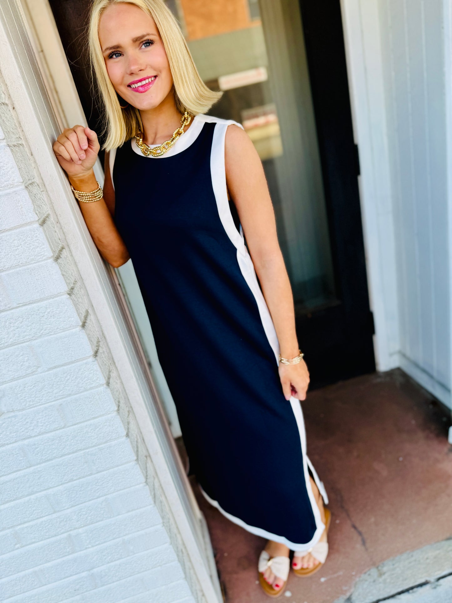 Woman wearing navy blue sleeveless maxi dress with white trim, gold jewelry, and sandals