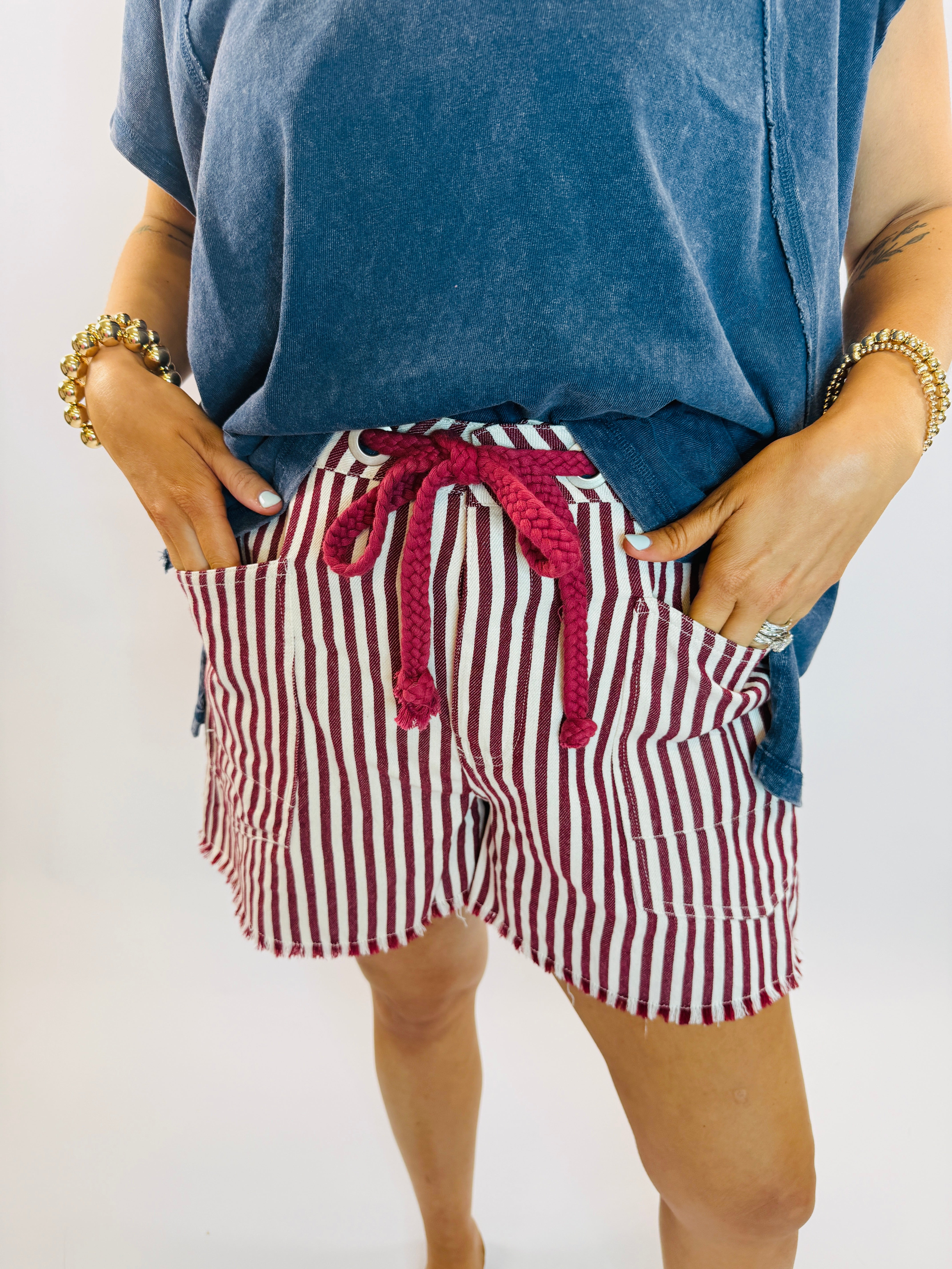 Red and white striped shorts with drawstring tie and frayed hem, styled with blue top and gold bracelets.