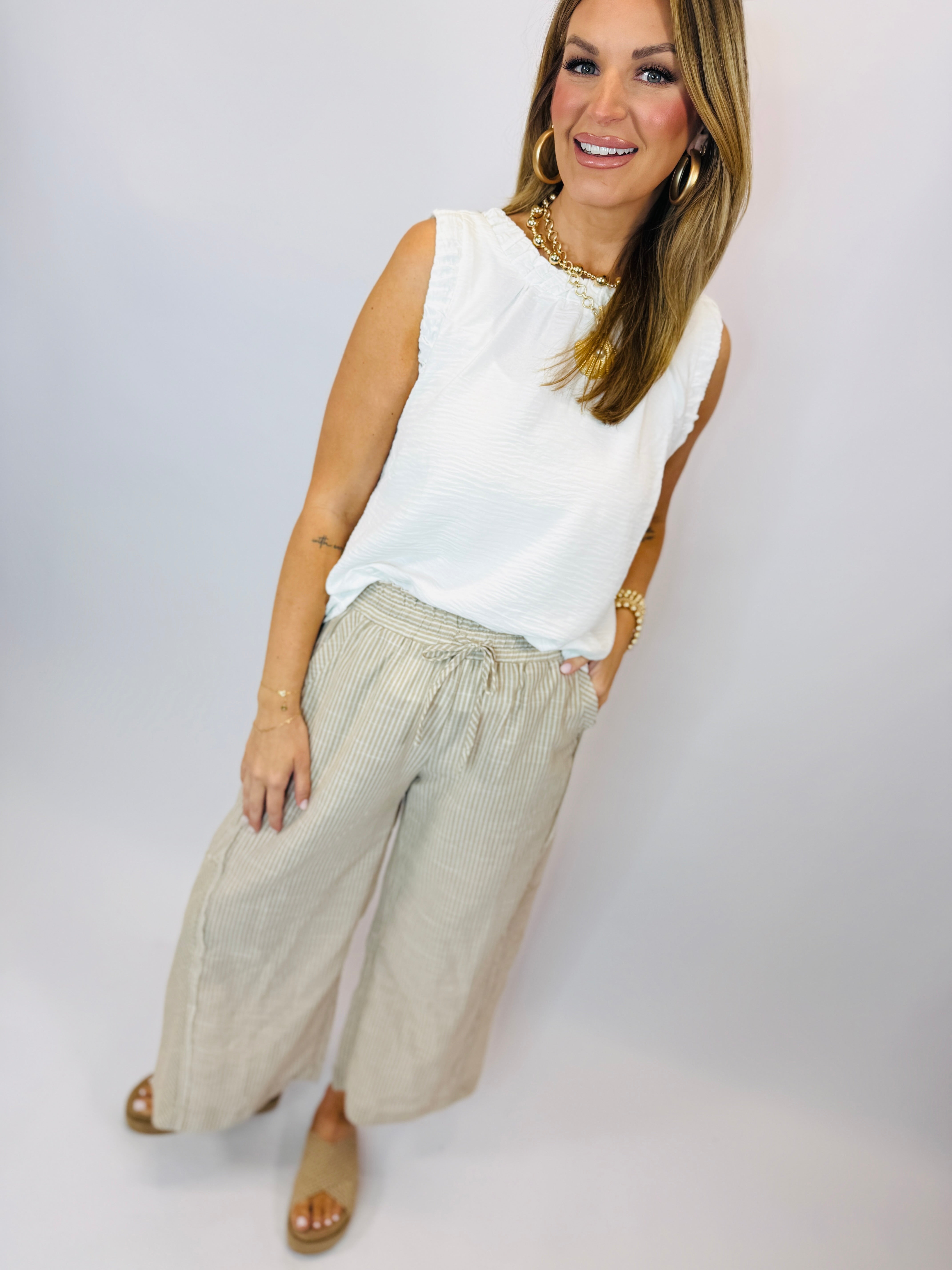 Woman wearing white sleeveless Darla tank top with light green striped wide-leg pants and gold jewelry.