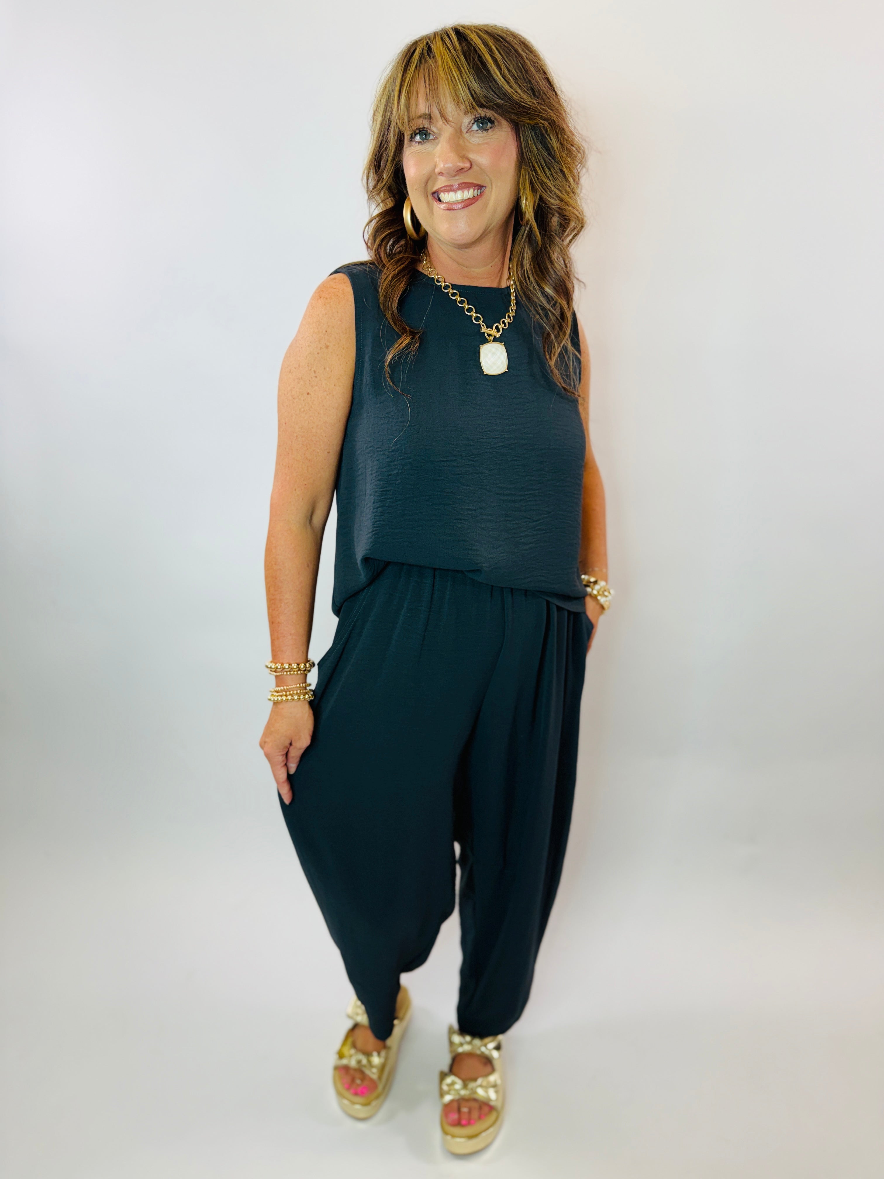 Woman wearing teal sleeveless top and matching cropped pants set with gold jewelry and sandals