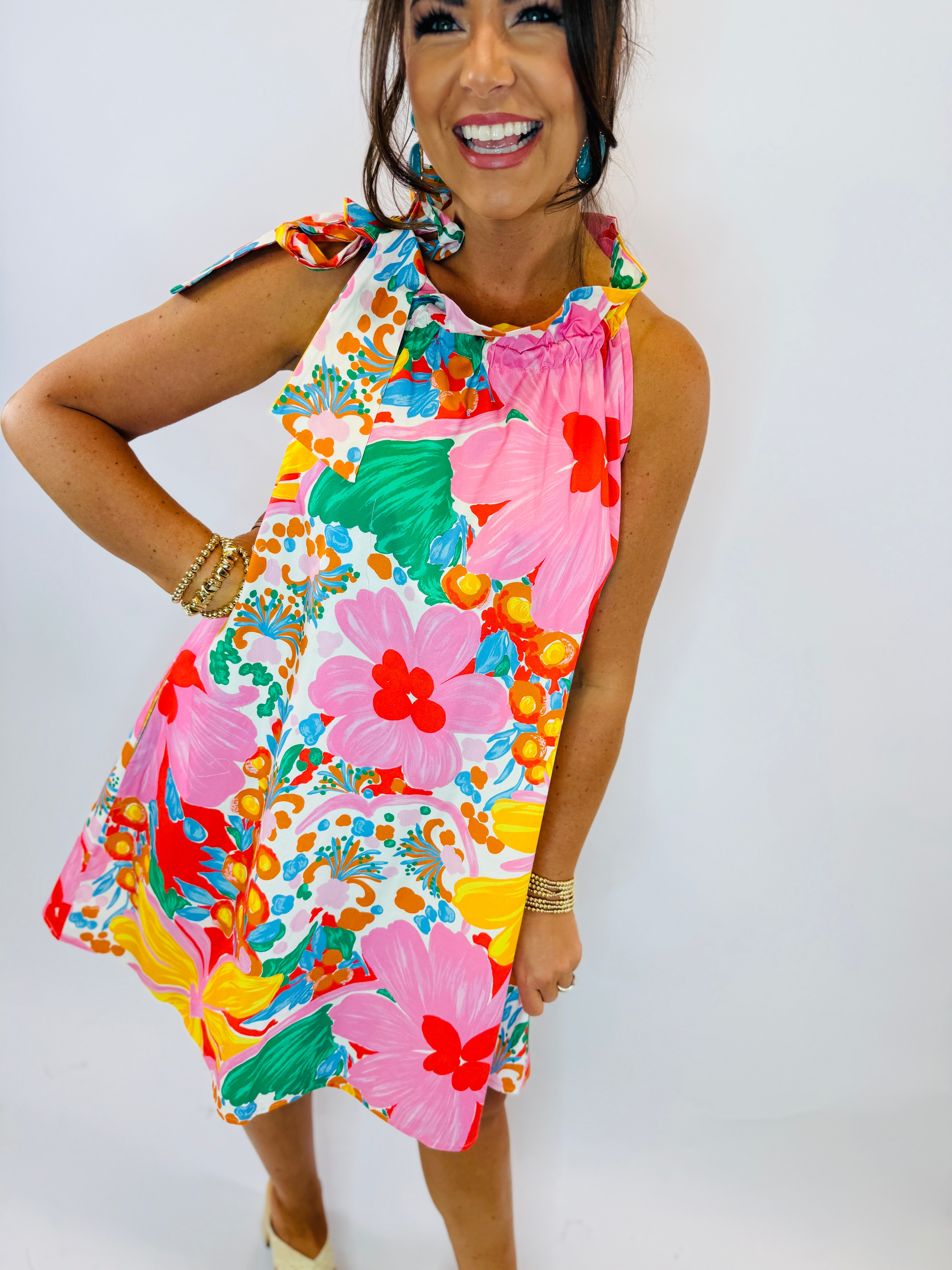 Woman wearing colorful tropical floral print sleeveless dress with tie shoulder straps and ruffled neckline