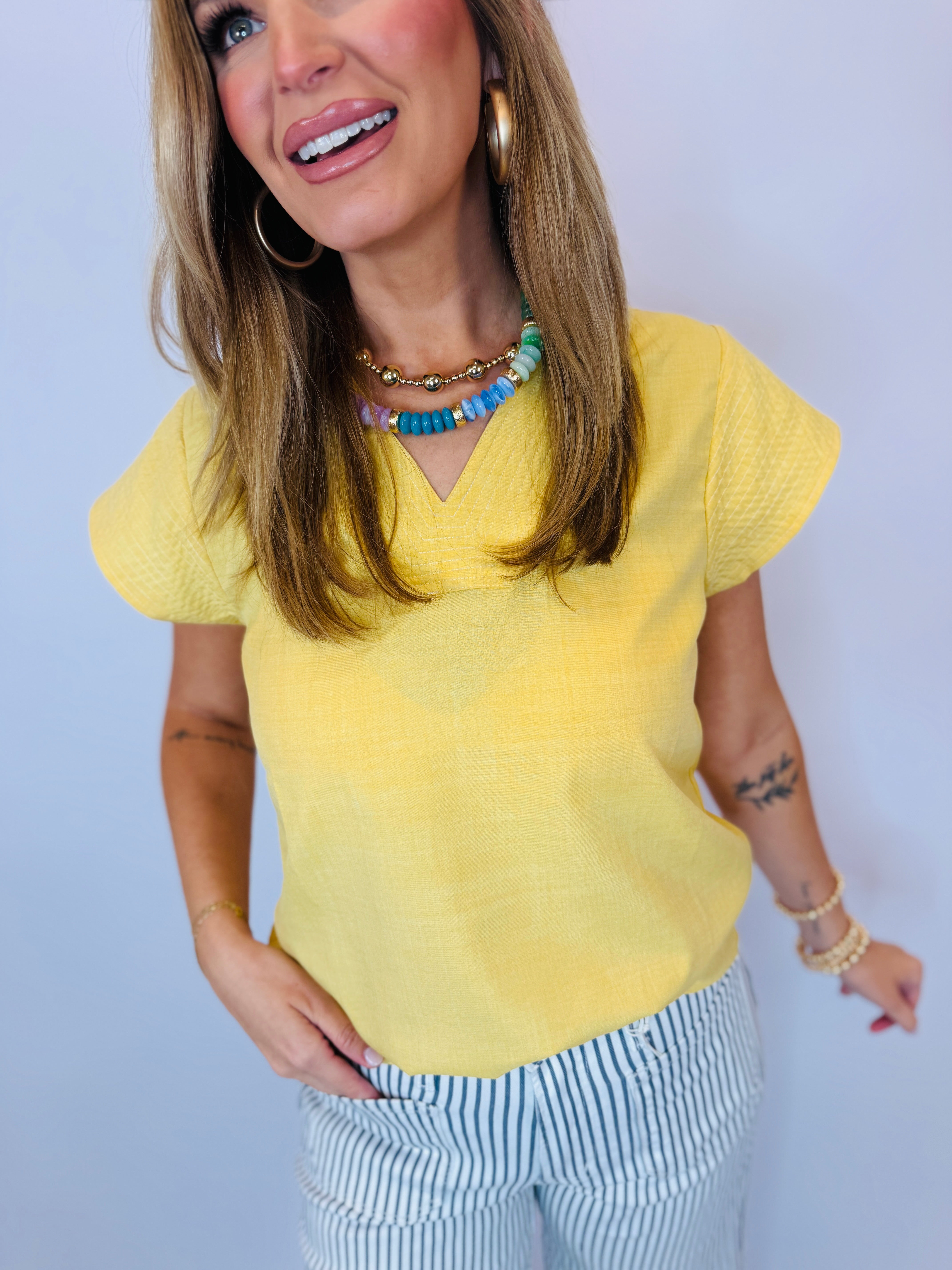 Woman wearing yellow v-neck Tracy Tank with flutter sleeves, paired with blue and white striped pants.