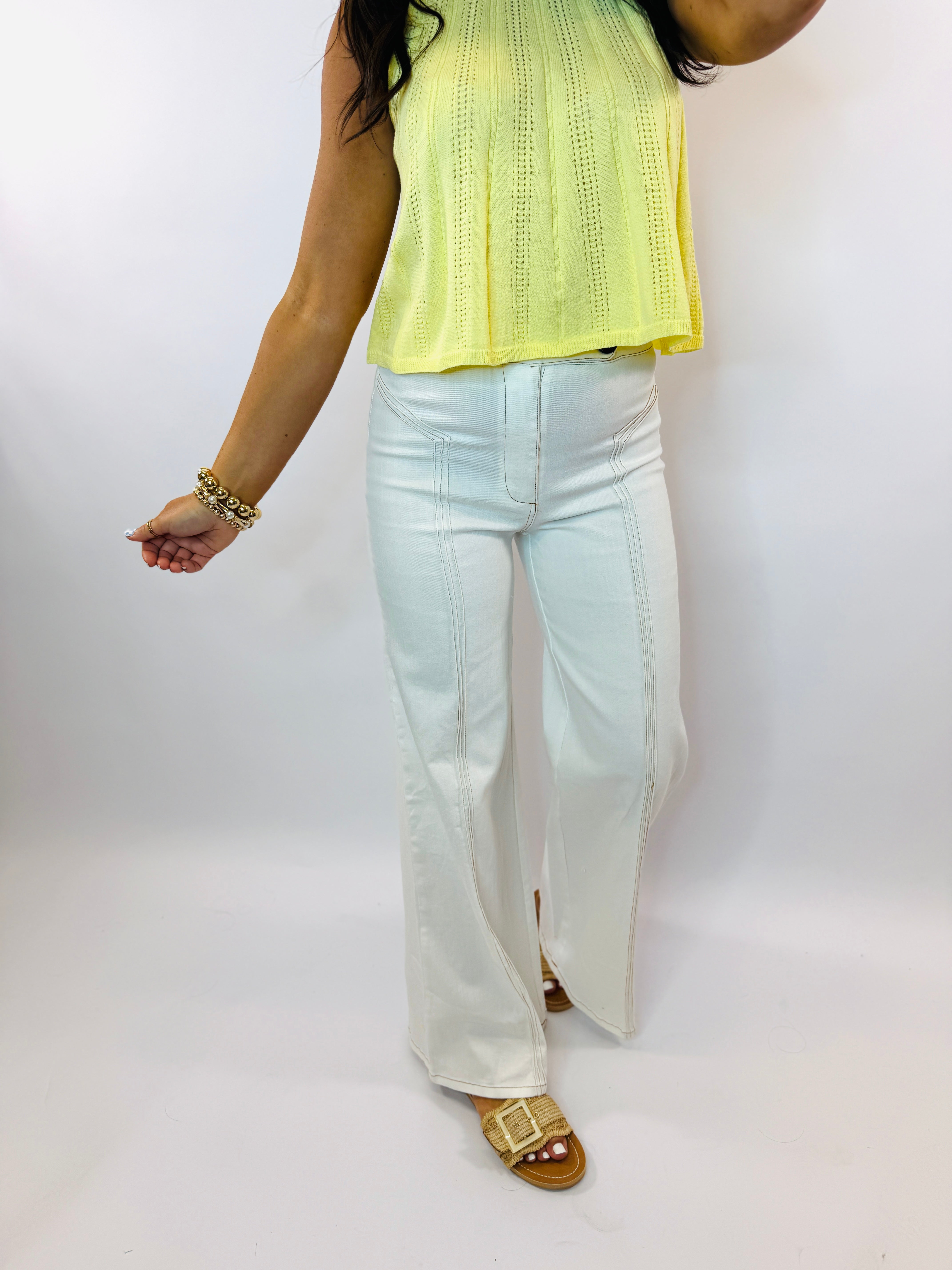 Light blue denim flare jeans with contrast stitching worn with yellow knit top and gold sandals.