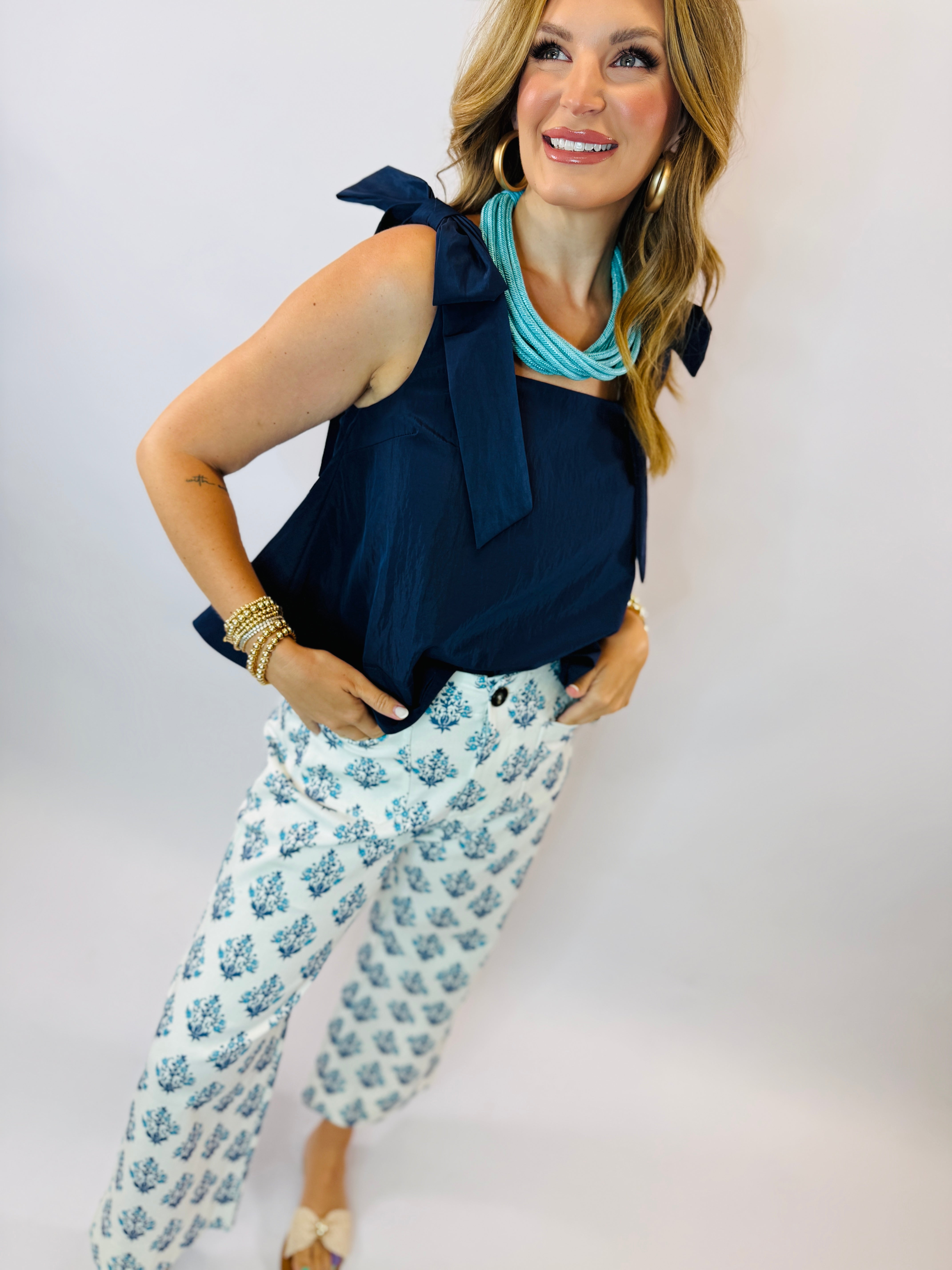 Woman wearing navy sleeveless bow tank top with white floral print pants and turquoise statement necklace