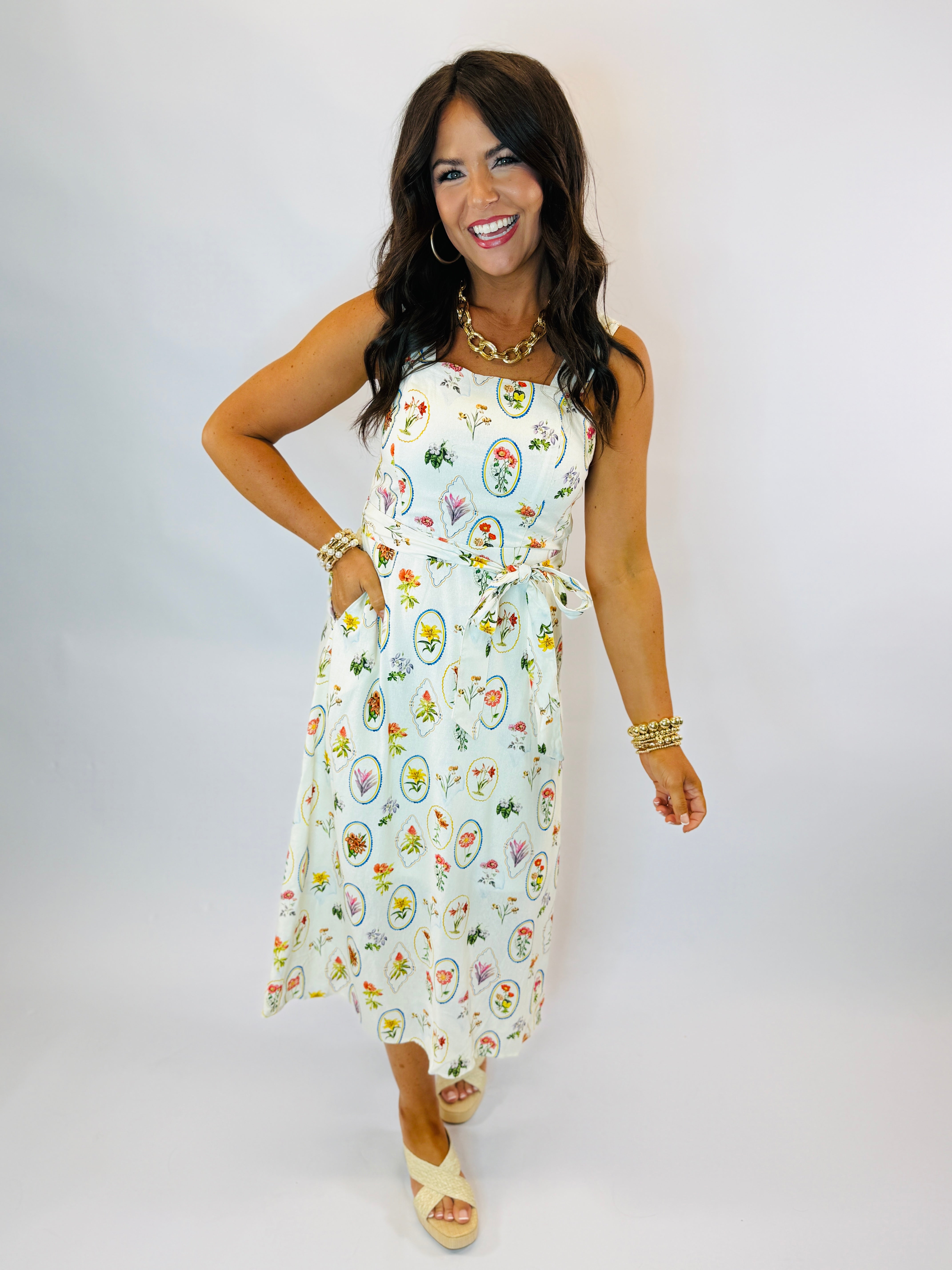 Woman wearing white floral midi dress with tie waist, gold jewelry, and platform sandals
