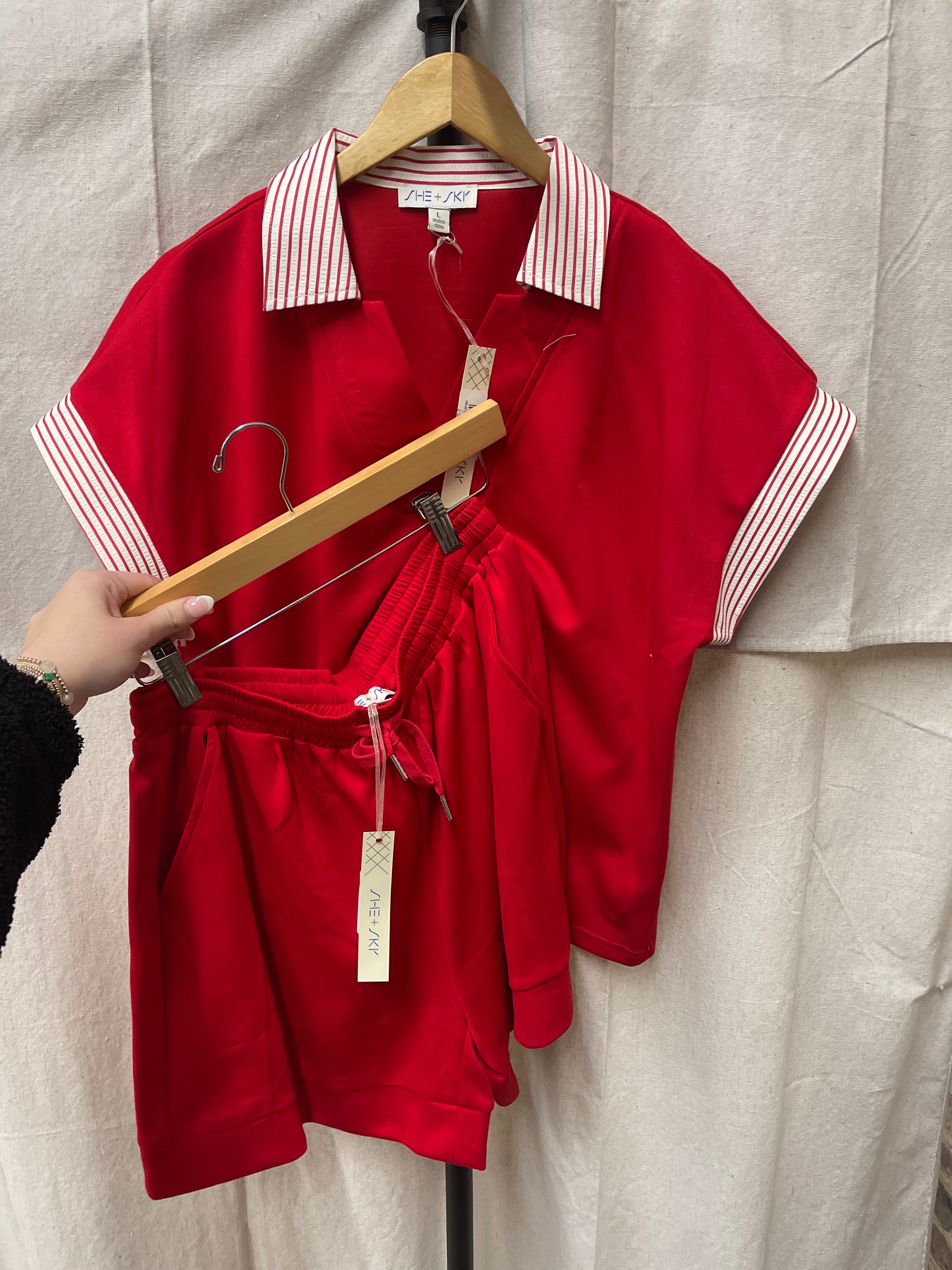 Red collared top with white striped trim and matching red shorts set displayed on wooden hangers