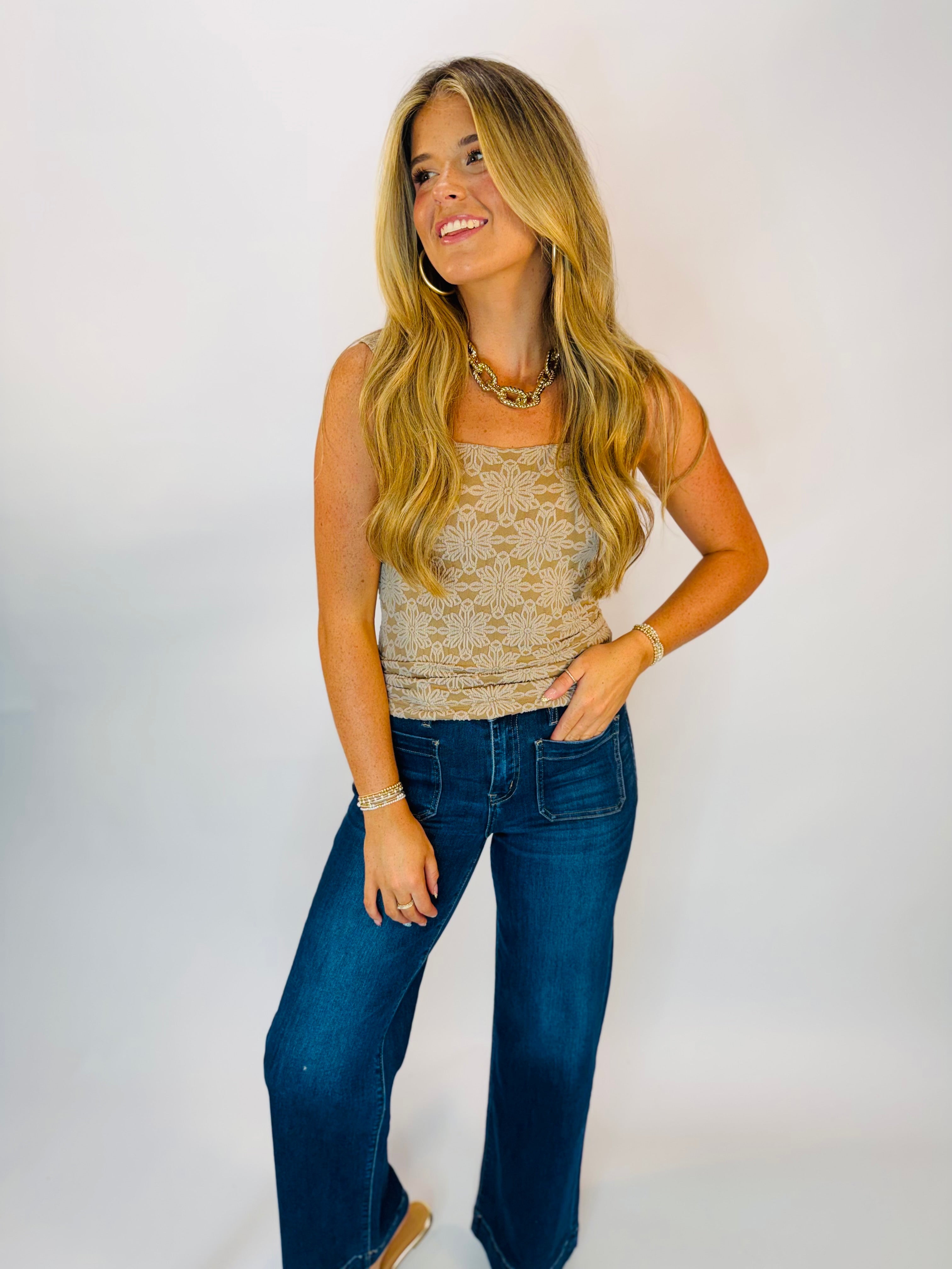 Woman wearing a tan floral lace sleeveless Hannah Tank top with dark blue wide-leg jeans.