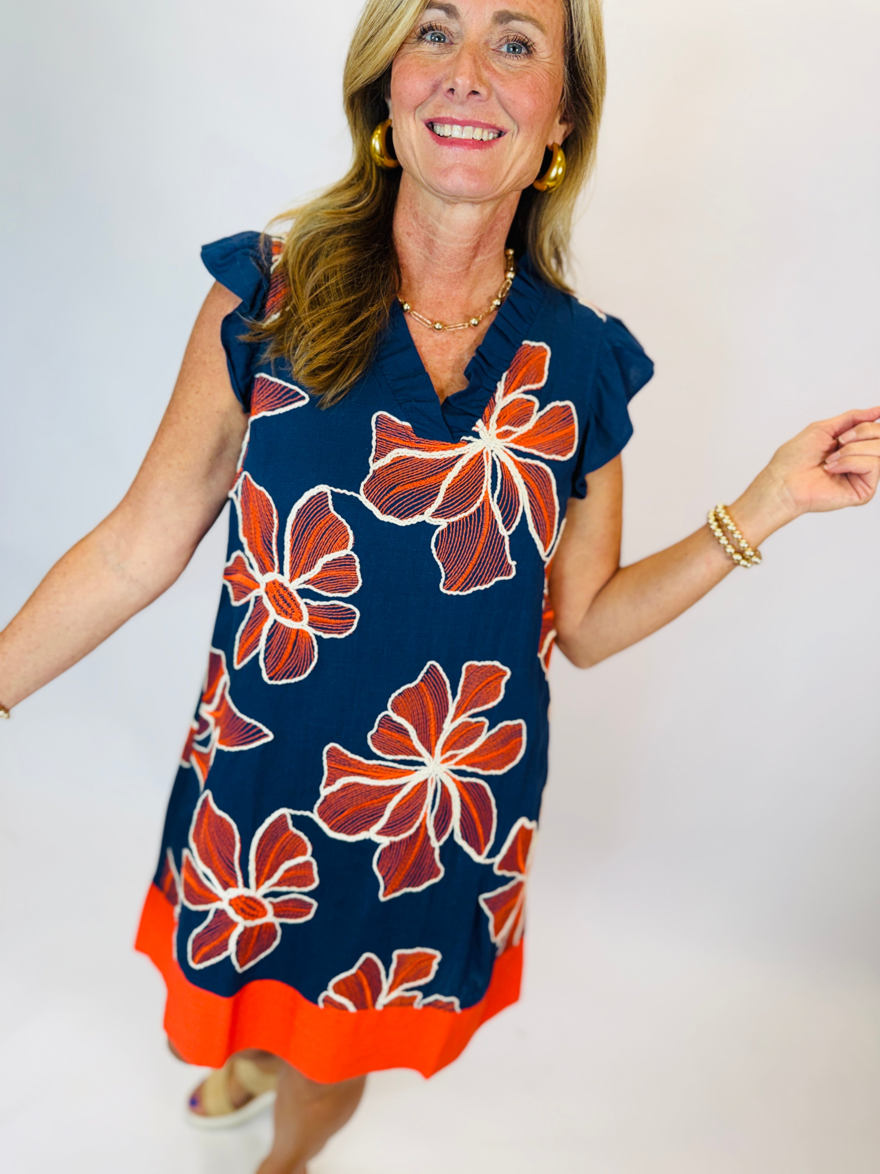 Navy blue floral embroidered Camry dress with orange border, flutter sleeves, and V-neckline on model.
