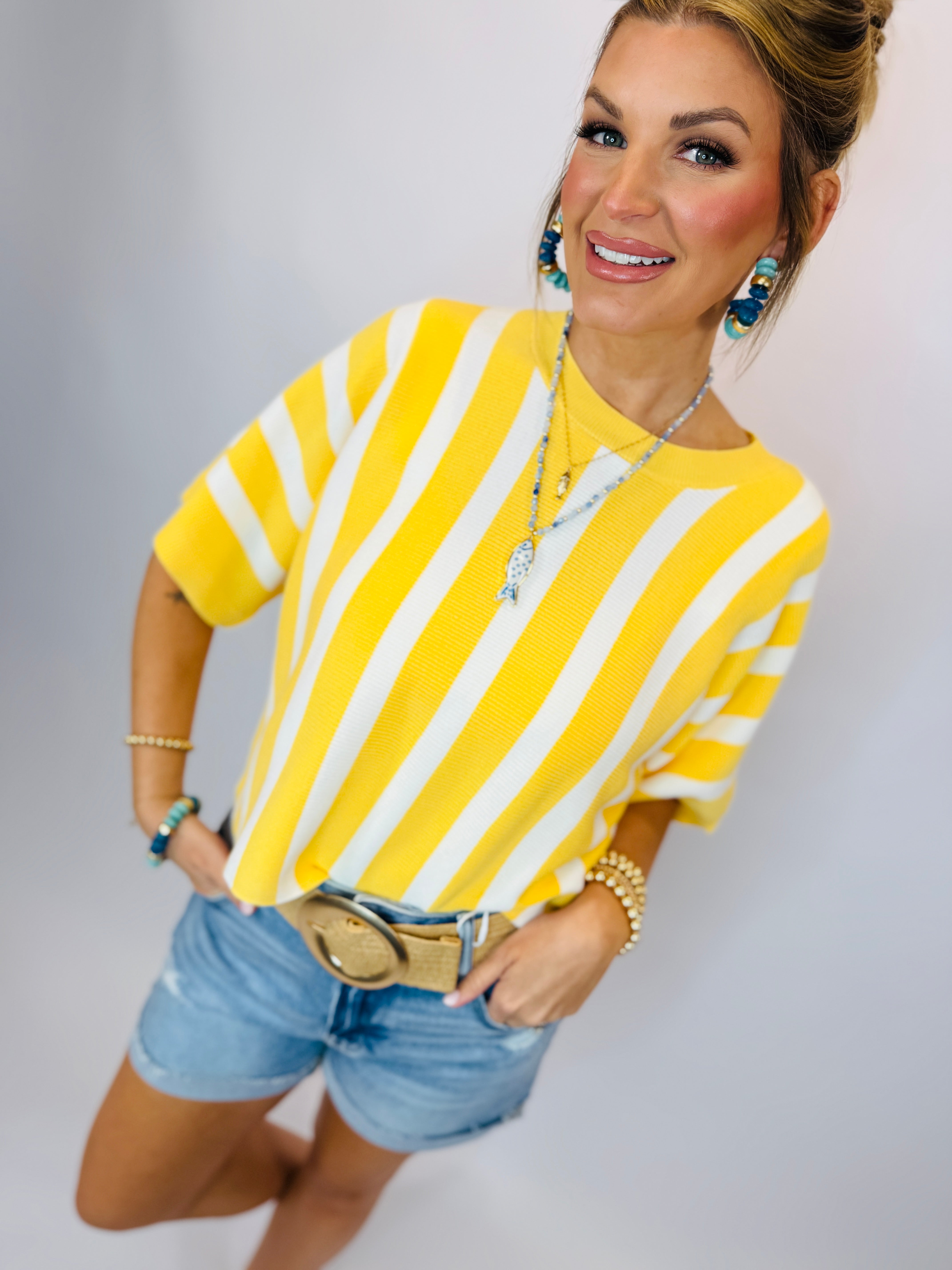 Woman wearing yellow and white striped short-sleeve top with denim shorts and turquoise jewelry accessories.