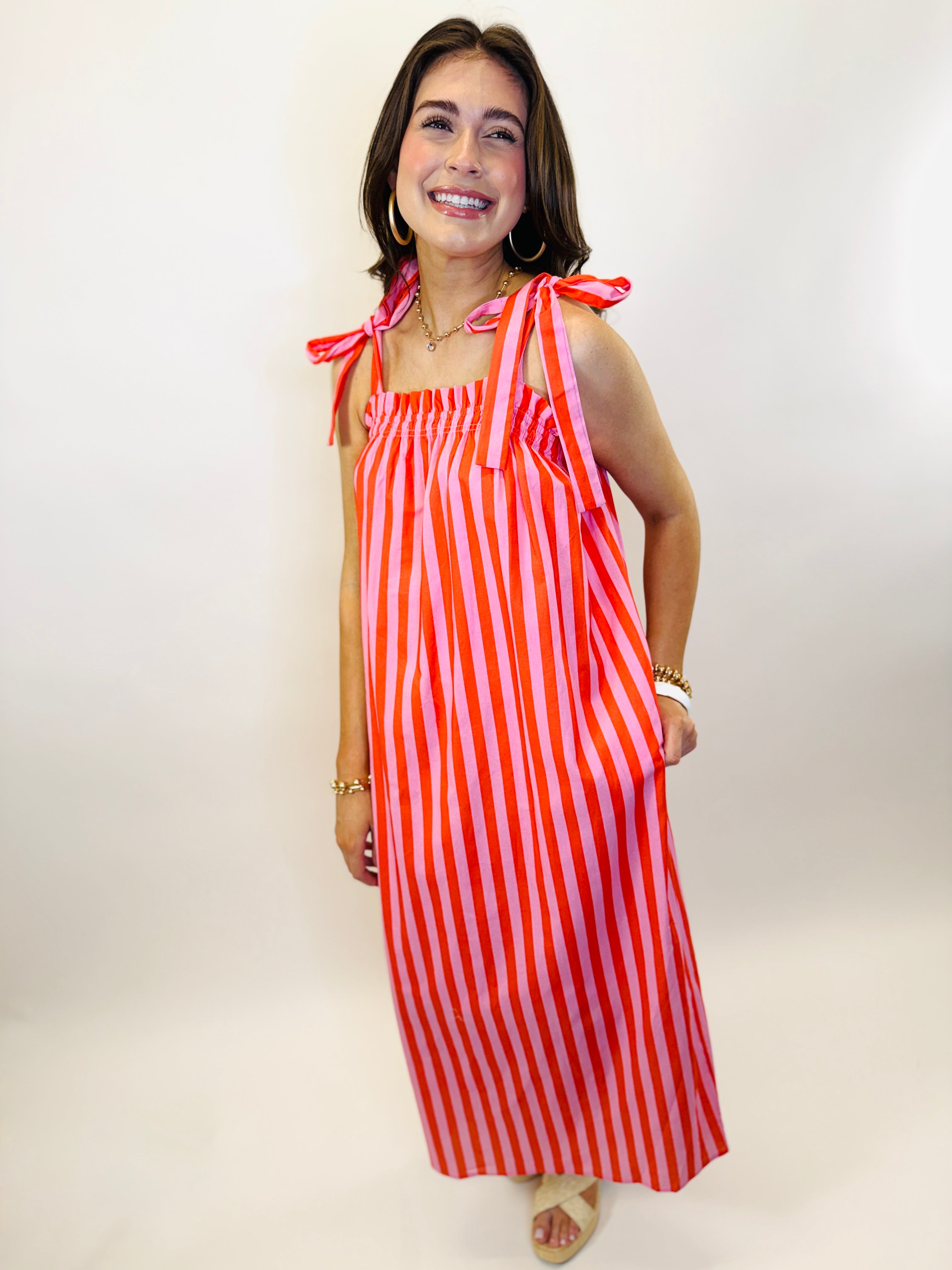 Woman wearing red and pink striped midi dress with tie shoulder straps and smocked bodice