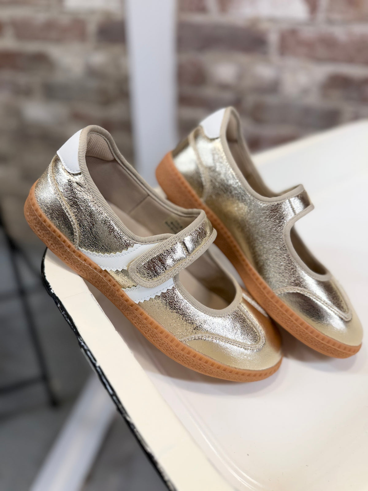 Gold metallic Mary Jane sneakers with elastic strap, white accents, and caramel gum soles.