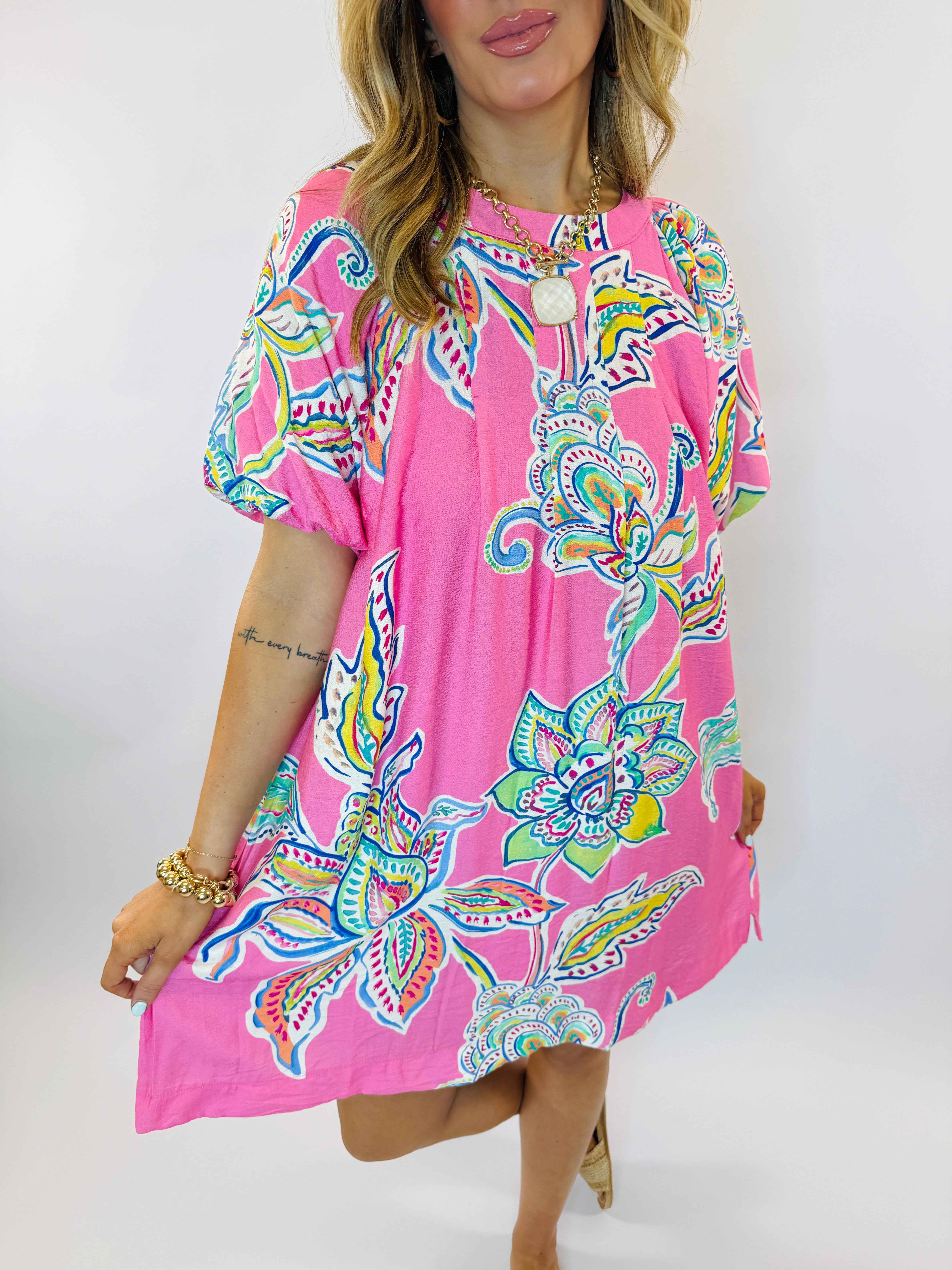 Woman wearing pink floral paisley print short-sleeve dress with colorful tropical pattern and gold chain necklace
