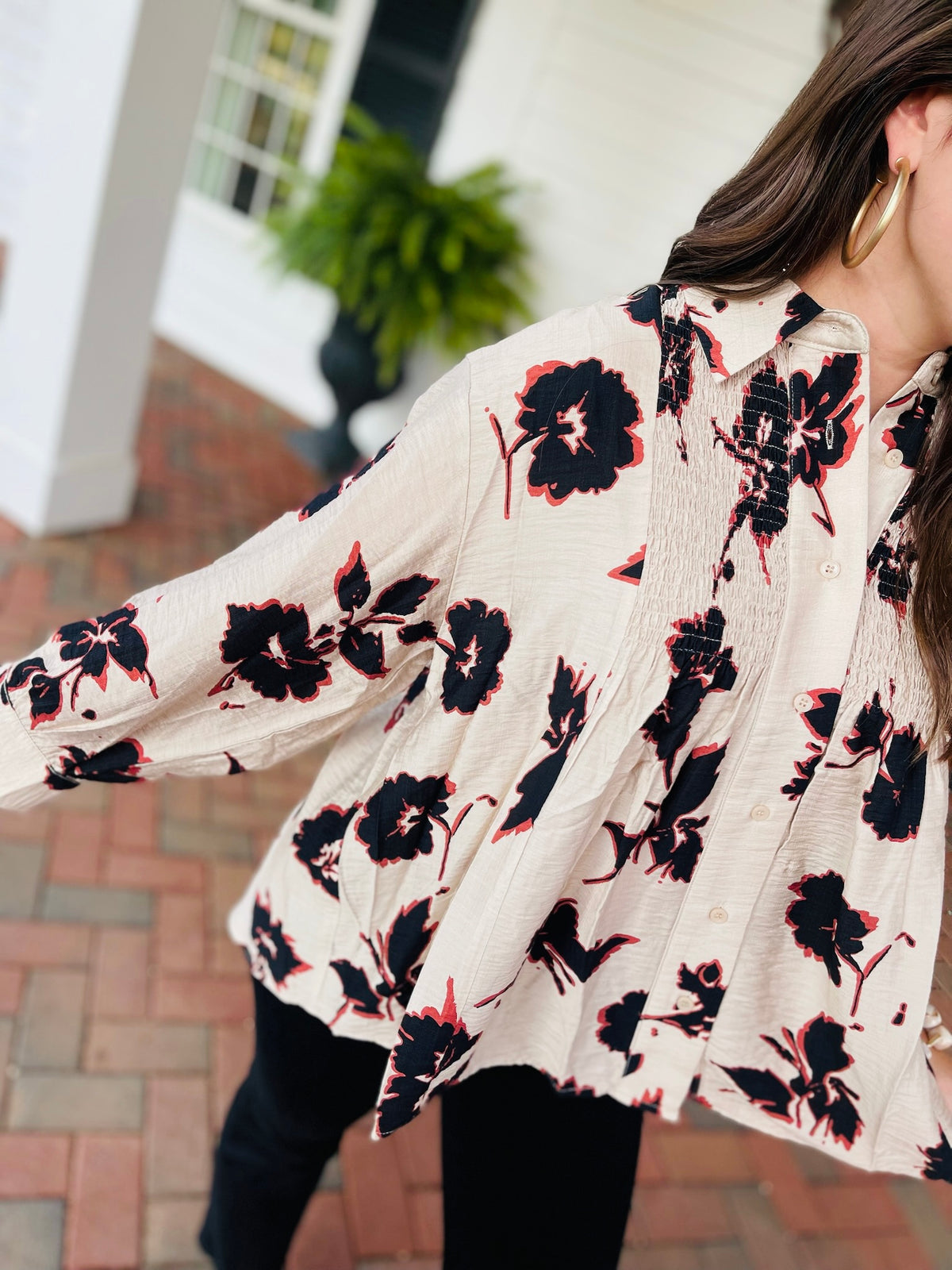 Detail of the Cora blouse, showing black flowers with coral accents on textured ecru fabric, front buttons, and gathered detailing.