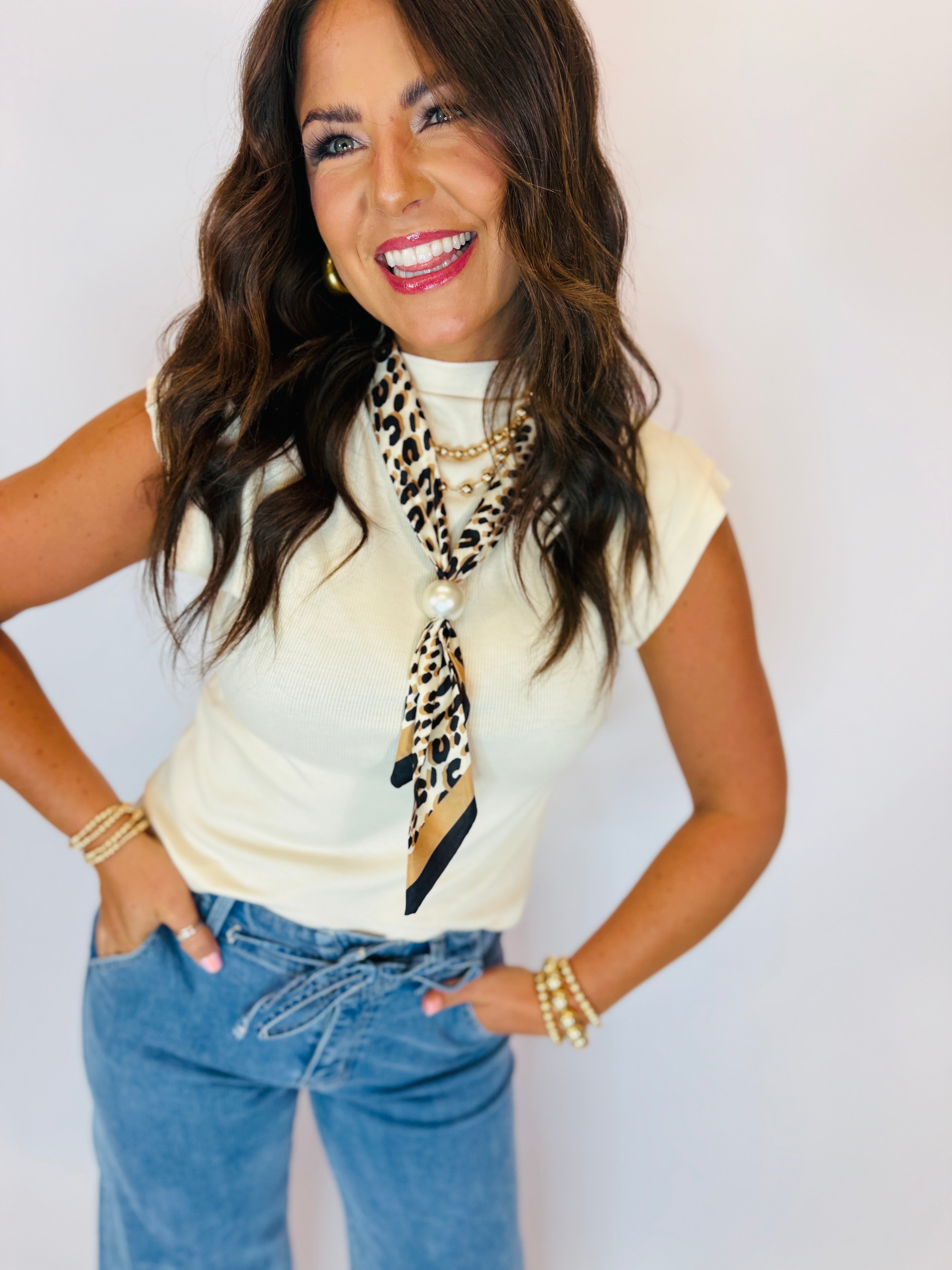 Ivory ribbed mock-neck cap-sleeve top styled with leopard scarf, pearl necklace, and blue jeans.