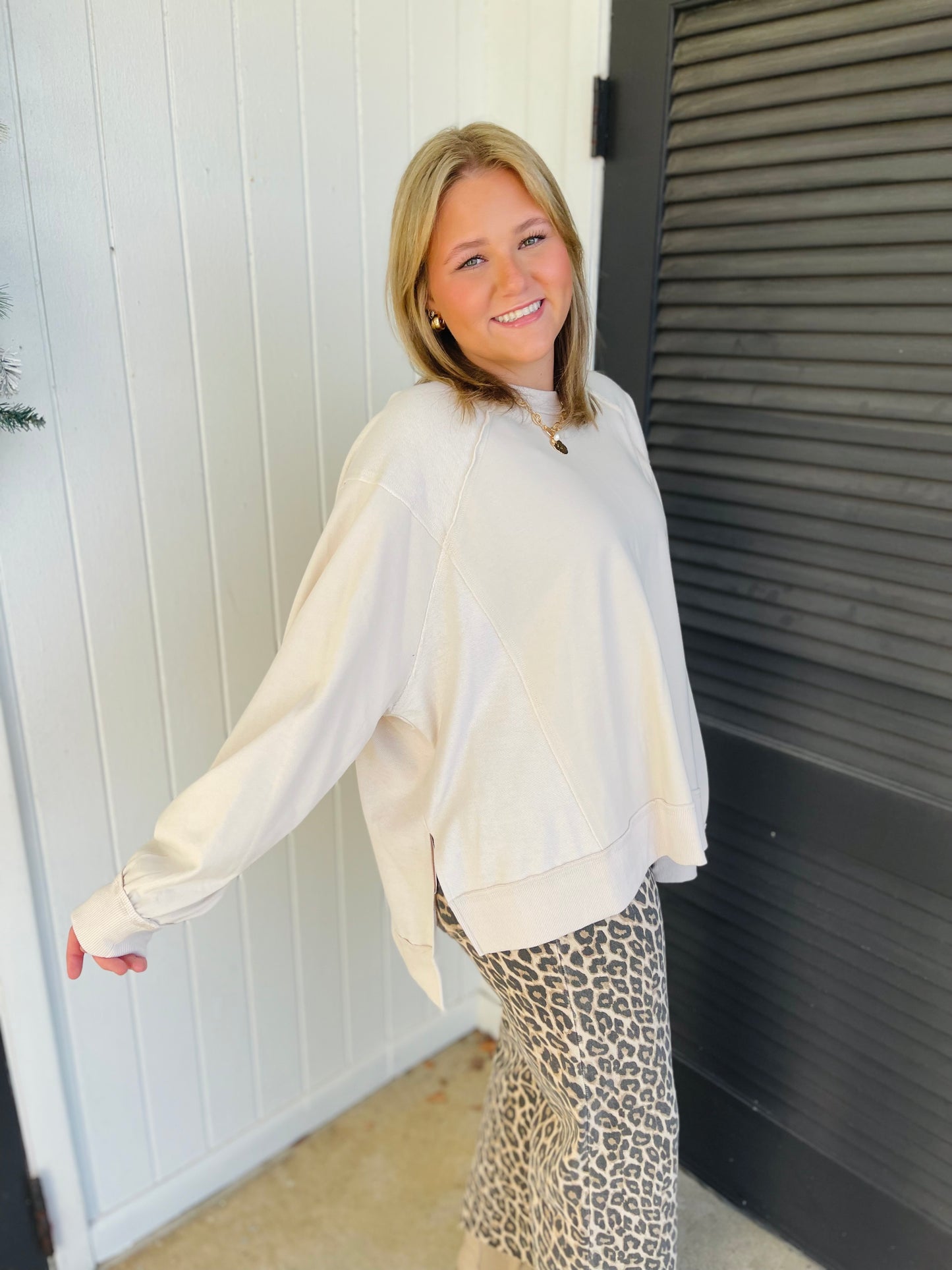 Woman wearing cream oversized sweatshirt with leopard print pants, smiling and posing casually