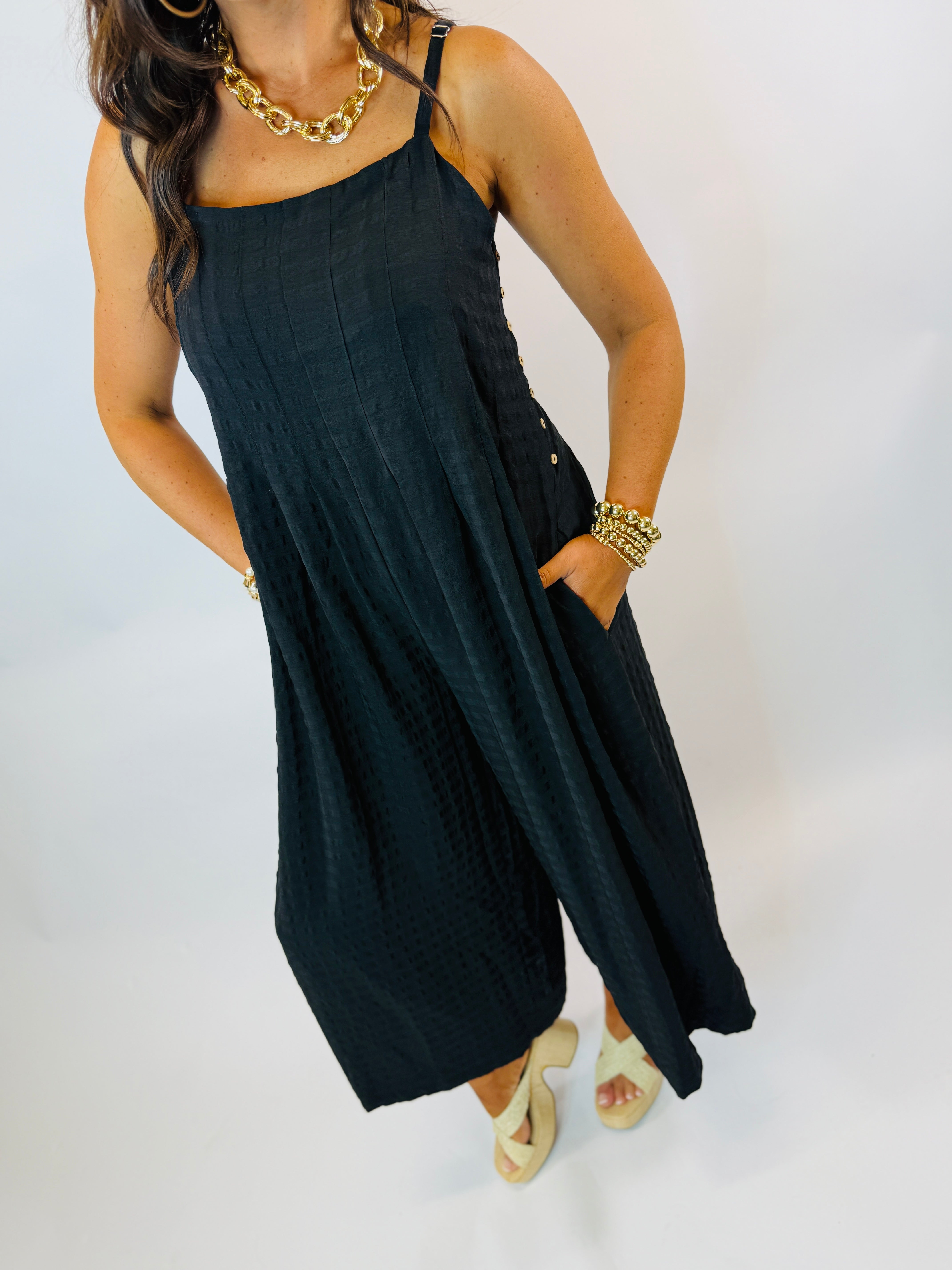 Woman wearing dark teal sleeveless wide-leg jumpsuit with gold jewelry and beige platform sandals