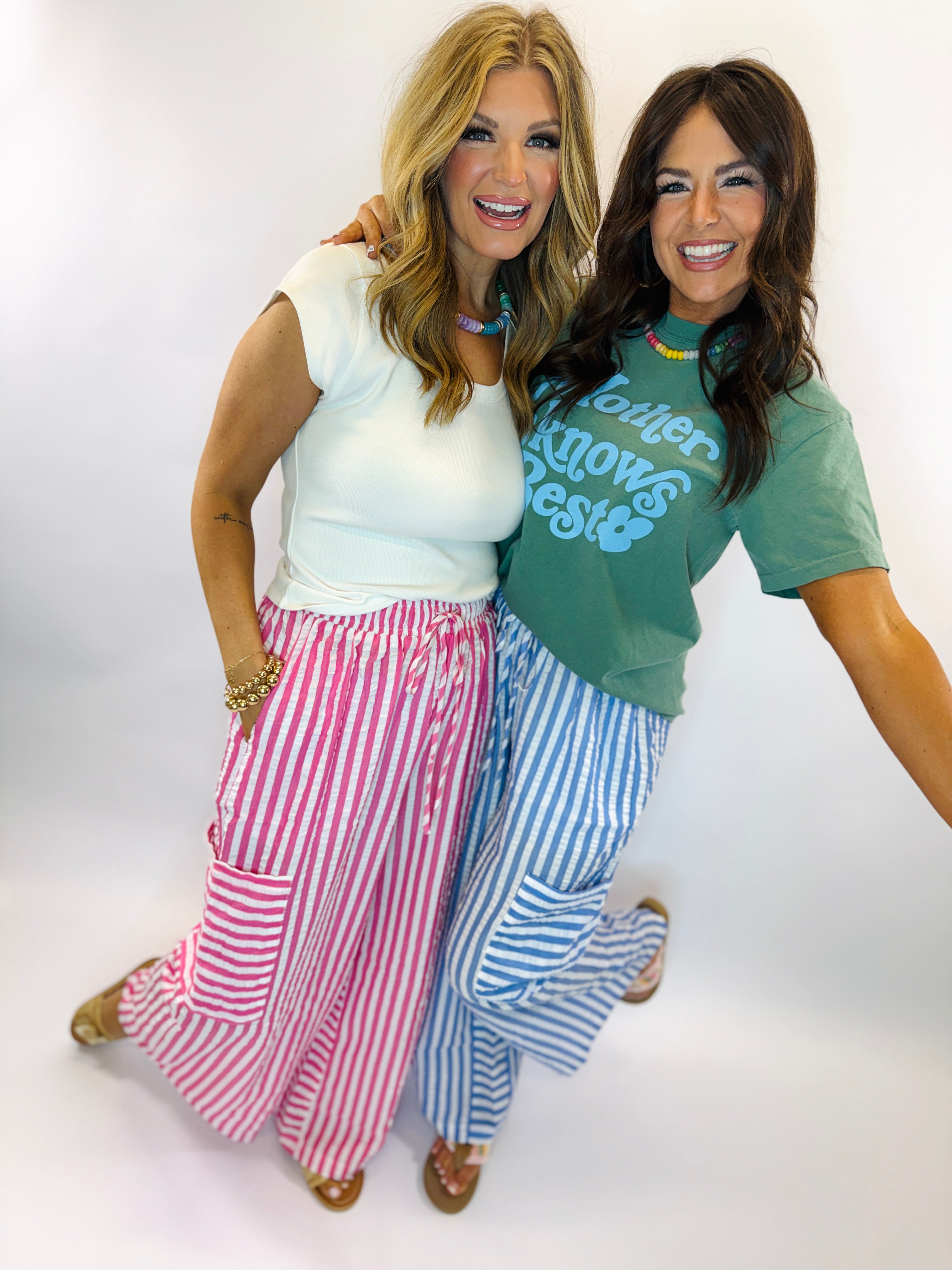 Two women wearing colorful striped wide-leg pants - one in pink stripes, one in blue stripes with coordinating tops.