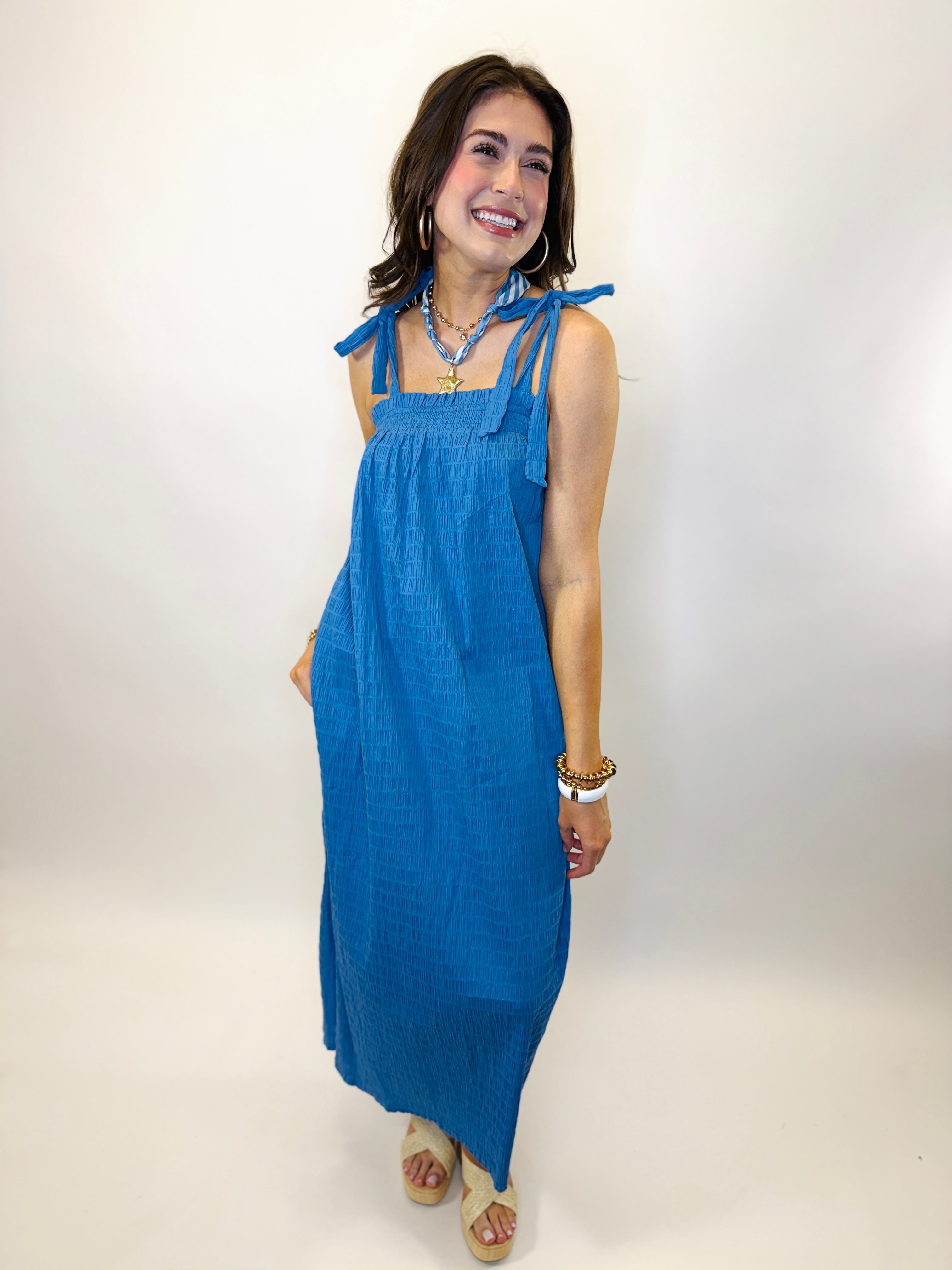 Woman wearing blue sleeveless maxi dress with tie shoulder straps and smocked bodice detail