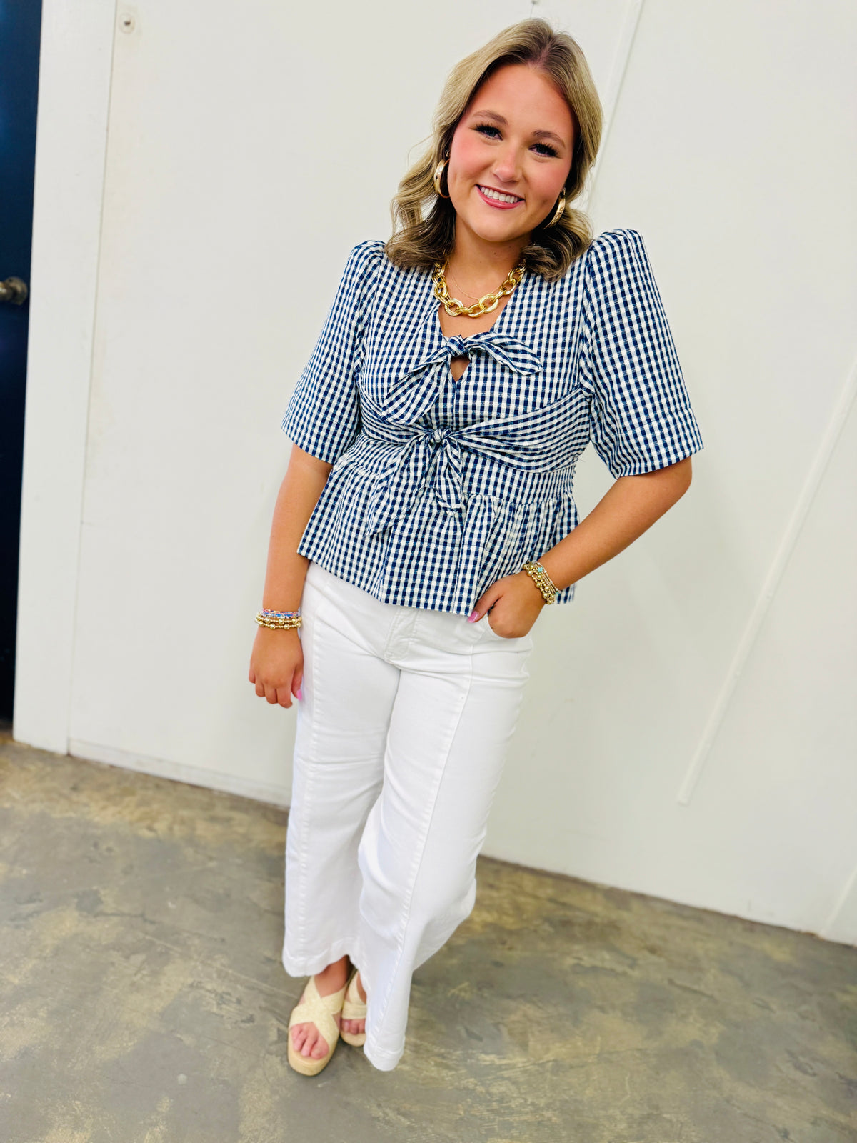 Woman wearing blue and white gingham tie-front top with white jeans and gold chain necklace