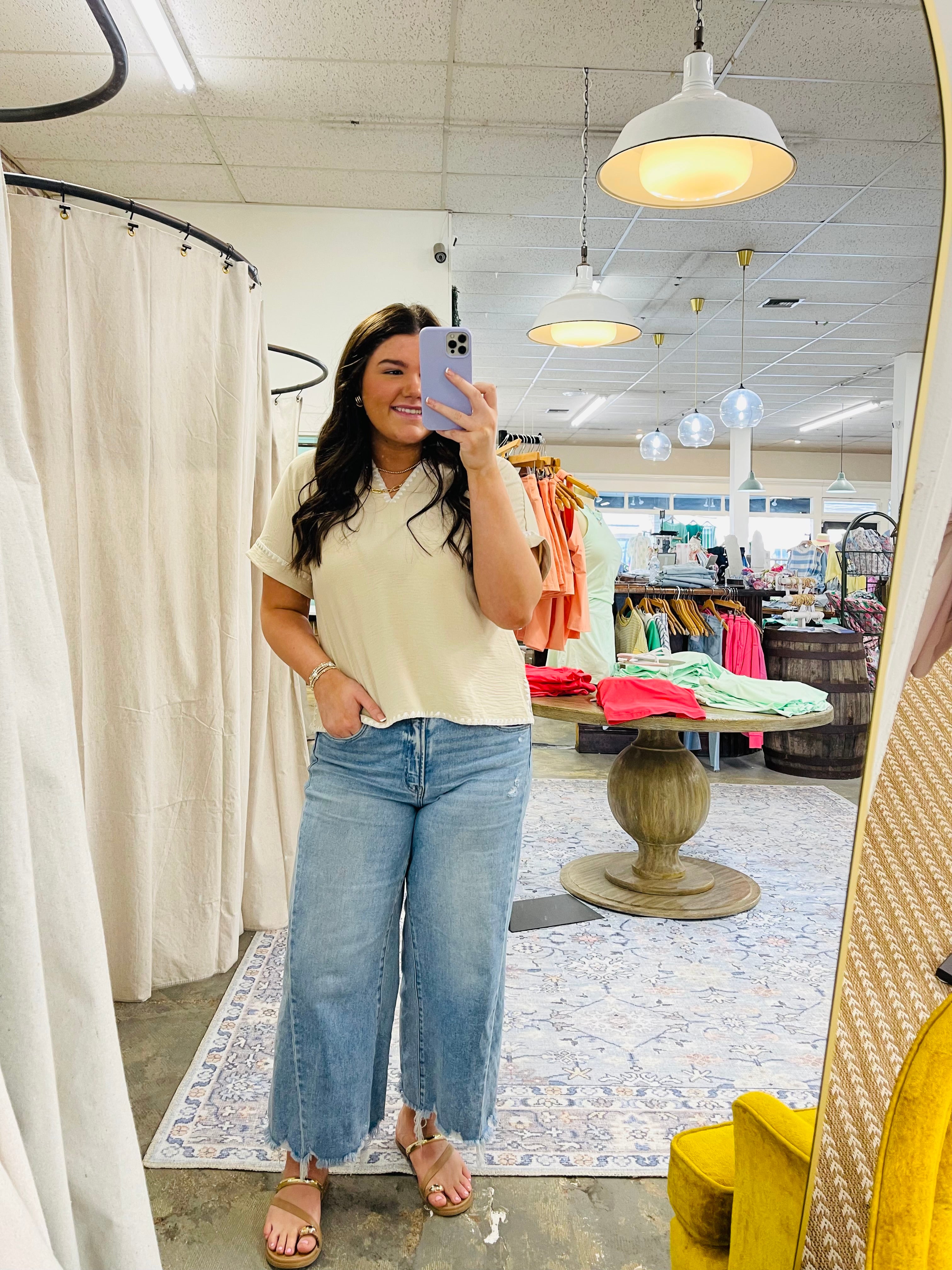 Woman wearing cream-colored Antonella top with wide-leg jeans, taking mirror selfie in clothing store