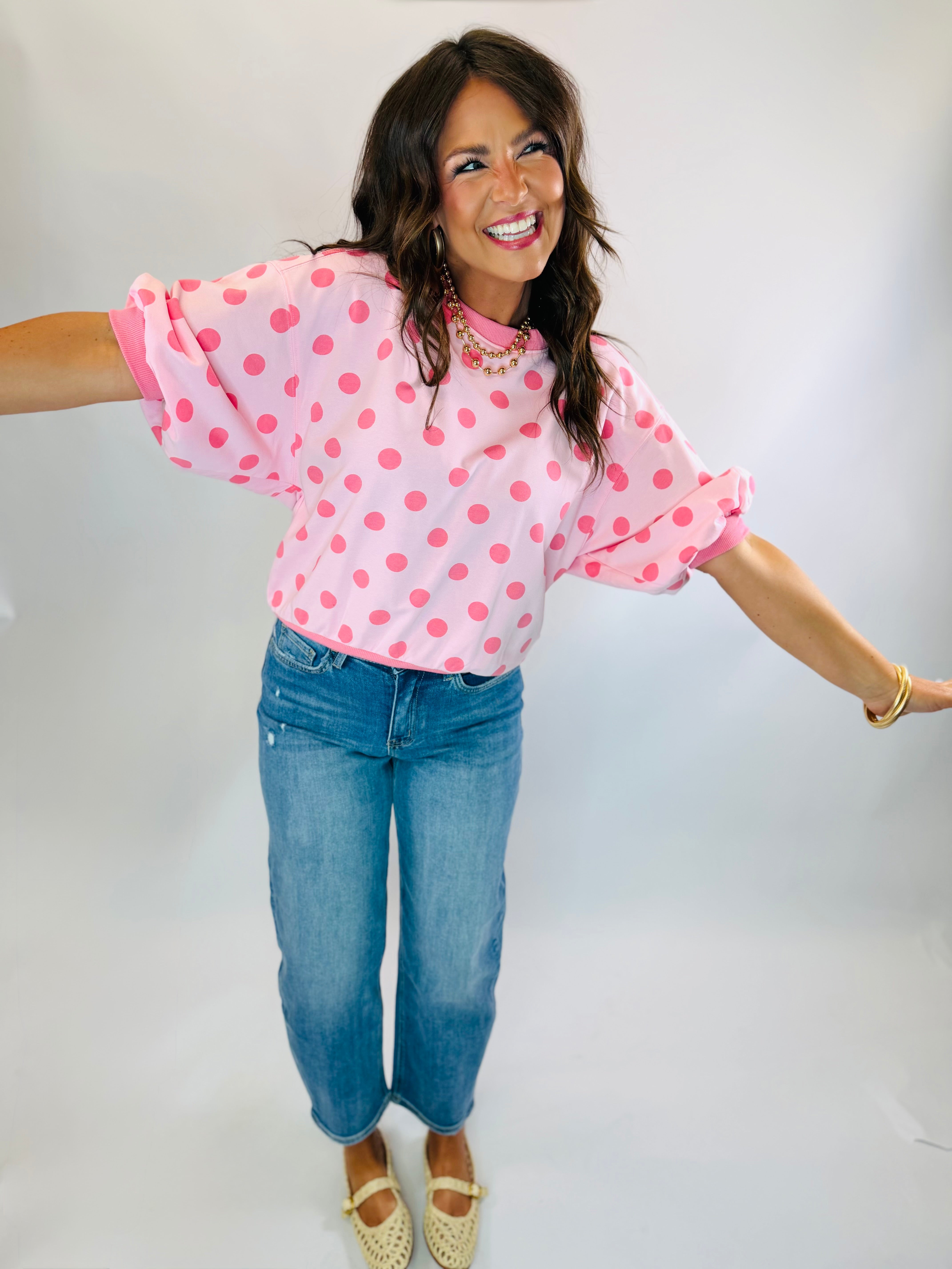 Woman wearing pink polka dot cropped sweatshirt top with rolled sleeves, paired with blue jeans.