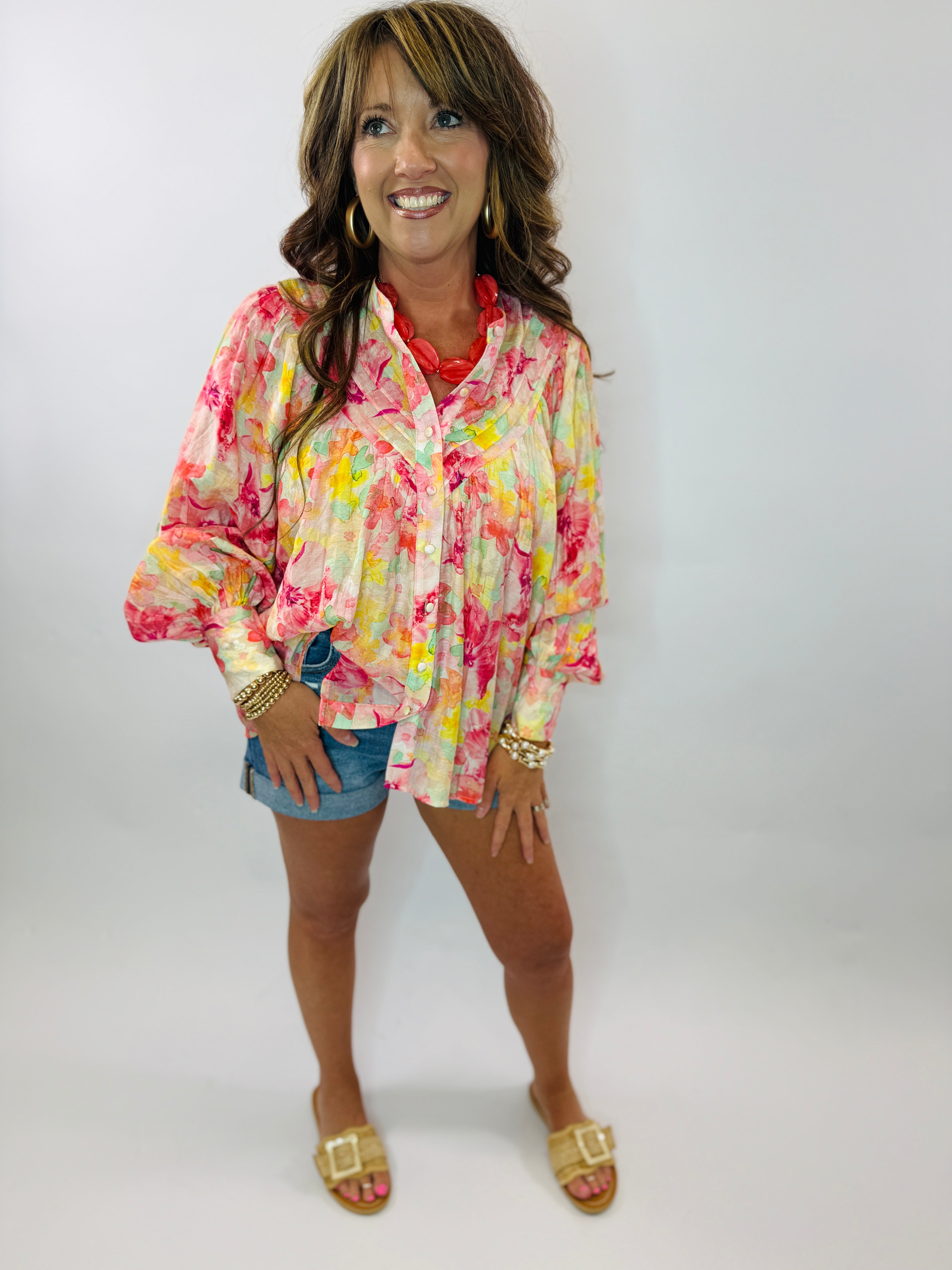 Woman wearing colorful floral button-up blouse with vibrant pink, yellow, and green pattern paired with denim shorts.