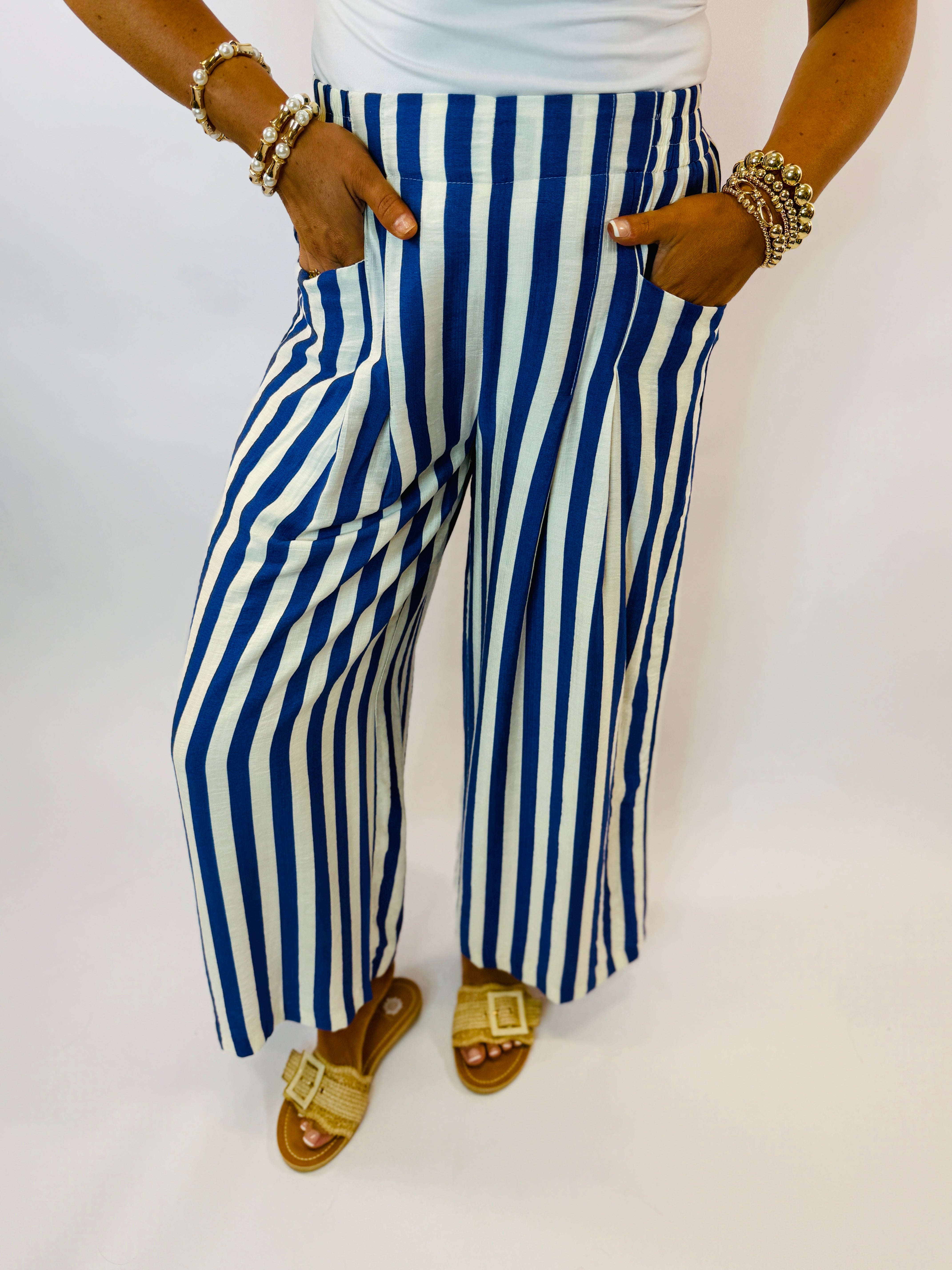 Woman wearing blue and white striped wide-leg pants with pockets, gold sandals and jewelry accessories.