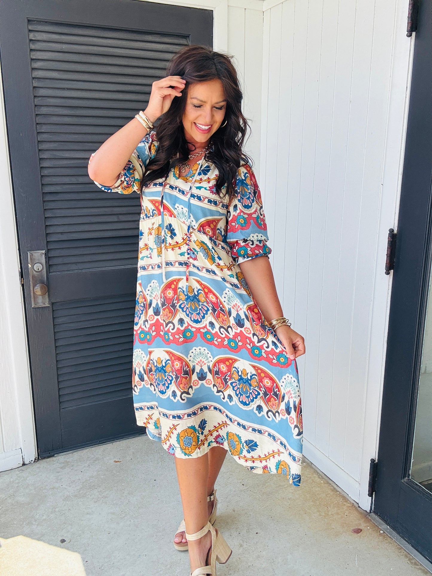 Woman wearing colorful paisley print midi dress with 3/4 sleeves, paired with tan block heel sandals.