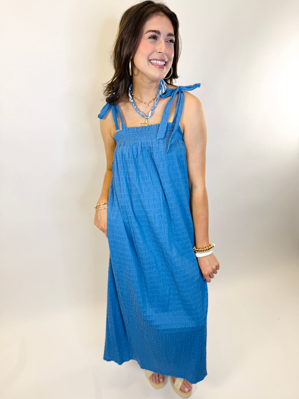 Woman wearing blue sleeveless maxi dress with tie shoulder straps and smocked bodice detail