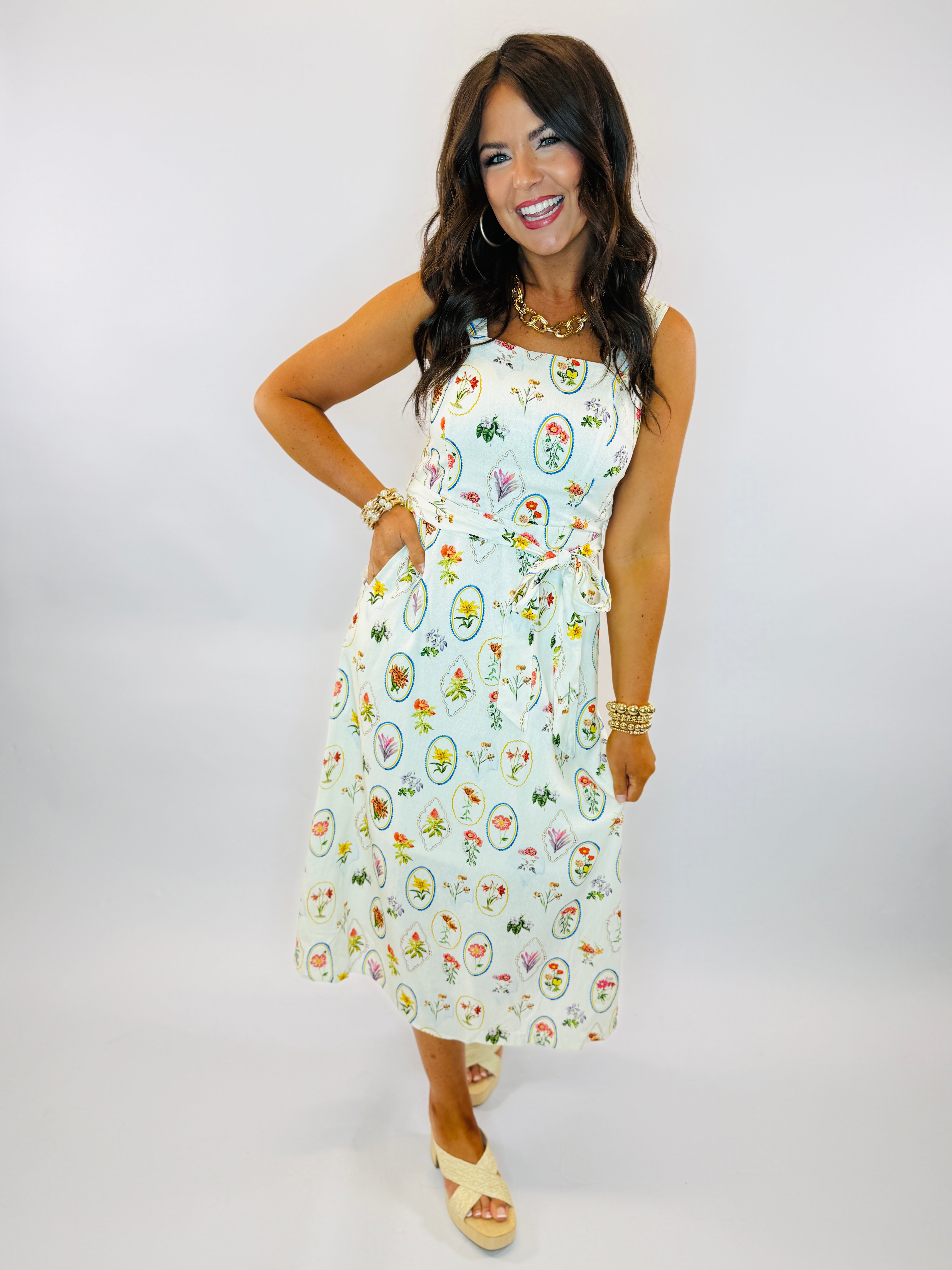 Woman wearing light blue sleeveless midi dress with colorful floral circle pattern and tie waist detail