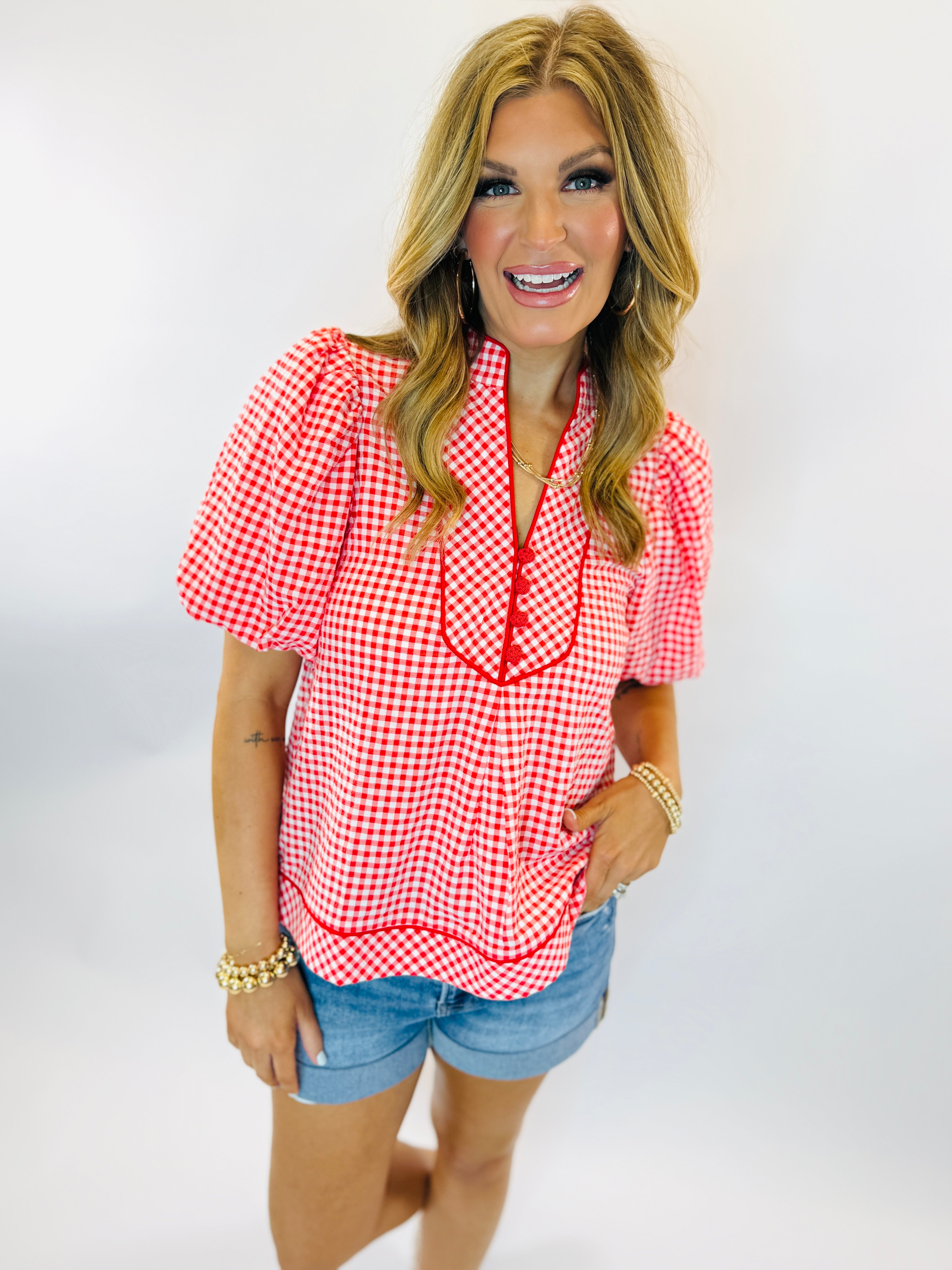 Woman wearing red and white gingham Diana top with short sleeves and button-front detail, paired with denim shorts.