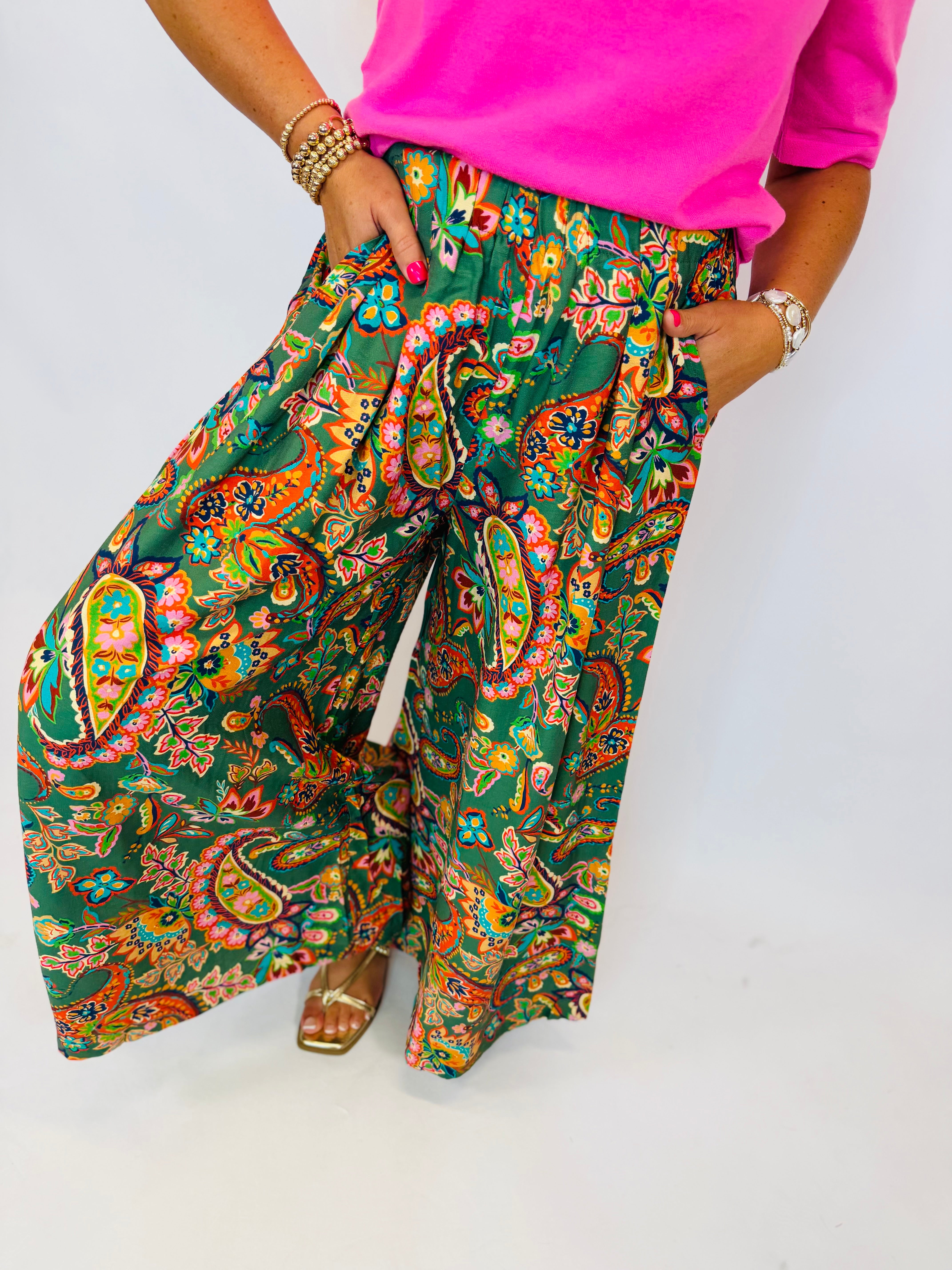 Callie printed wide leg palazzo pants in green paisley floral pattern, paired with hot pink top and gold sandals.