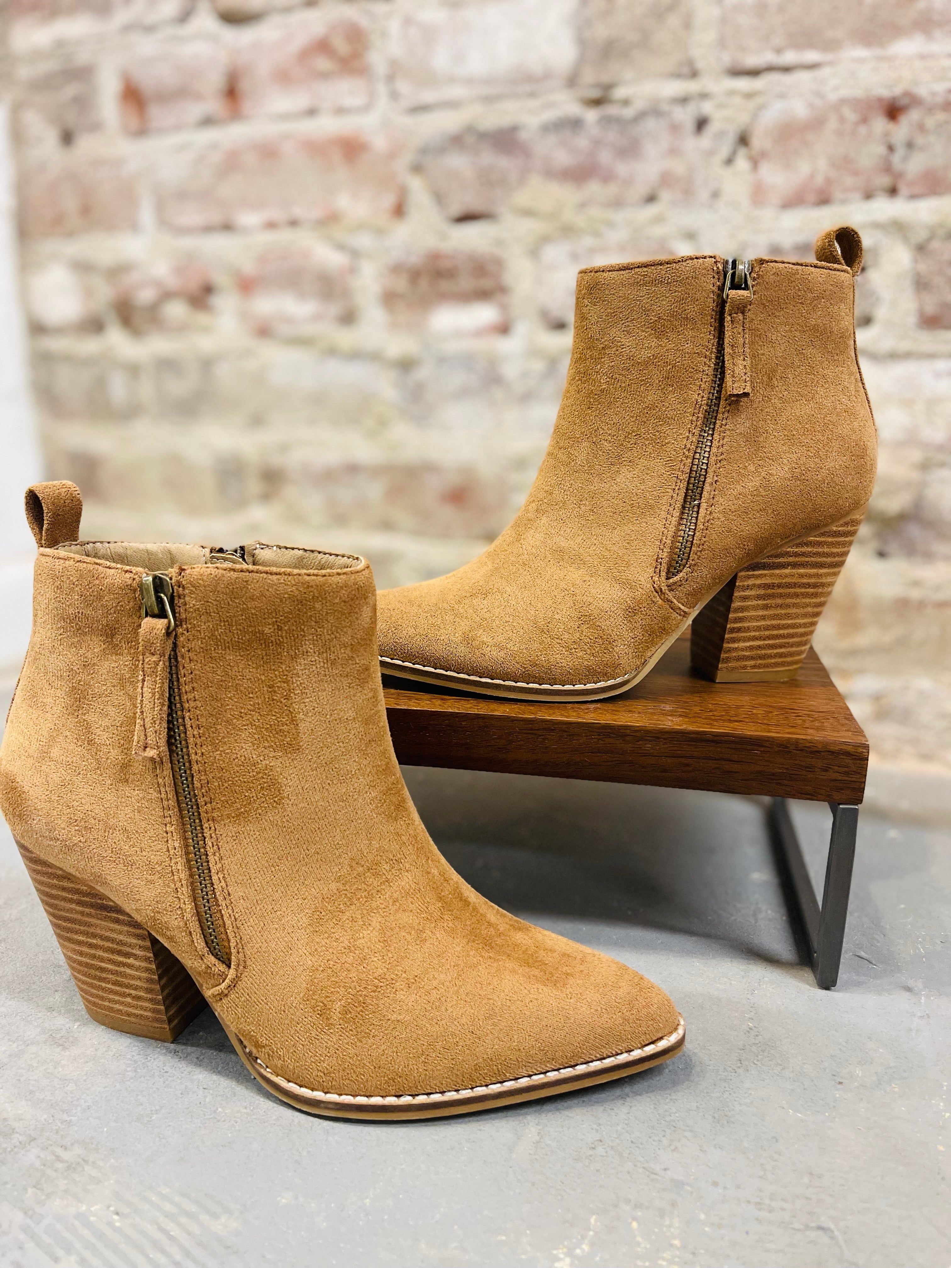 Tan faux suede ankle boots with block heels and side zippers displayed on wooden bench