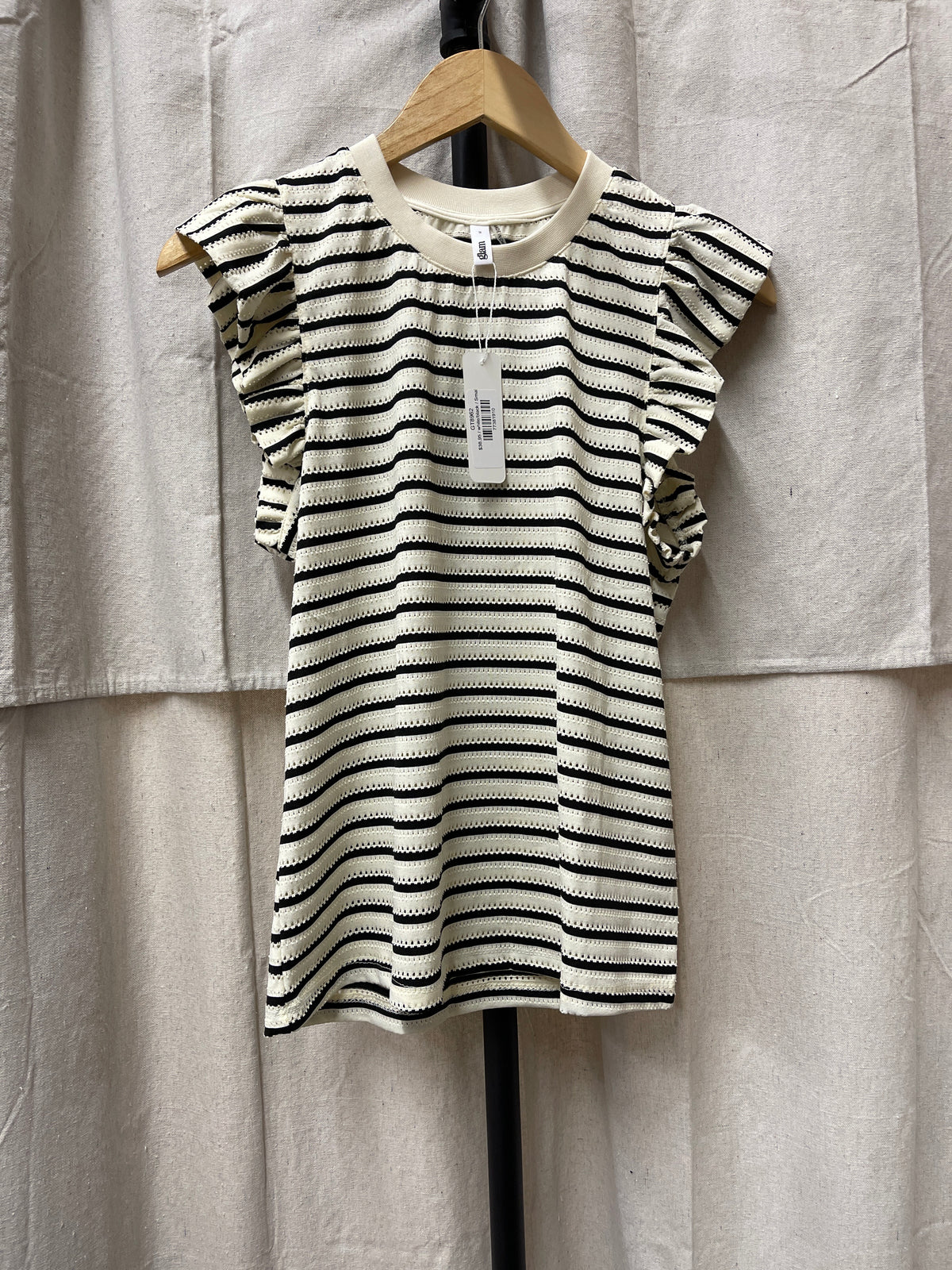 Striped knit top with ruffled short sleeves and crew neck hanging on wooden hanger against beige backdrop.