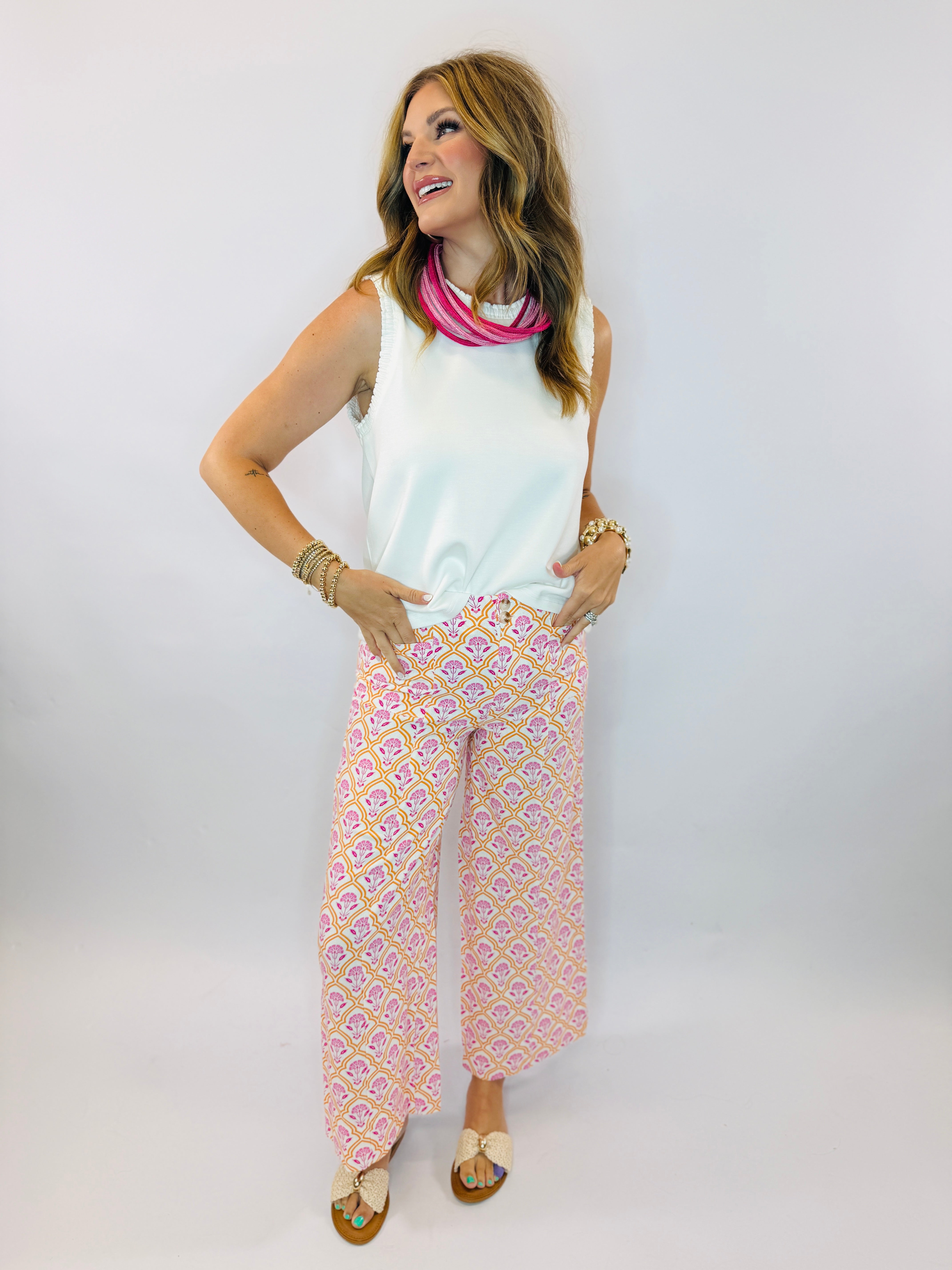 Woman wearing off-white sleeveless Georgie top with pink patterned wide-leg pants and layered jewelry accessories.
