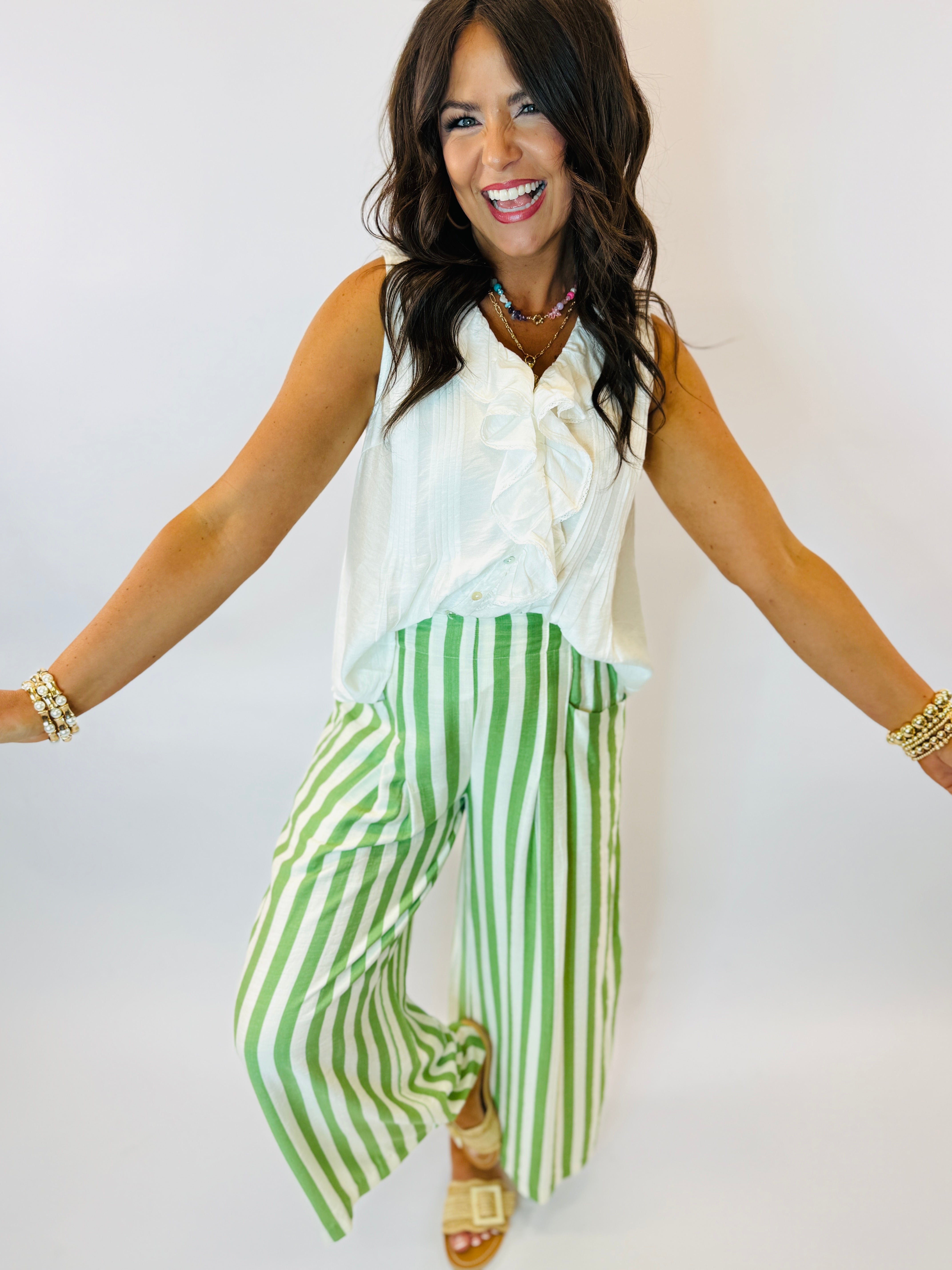 Woman wearing white sleeveless Ellis top with green and white striped wide-leg pants, smiling with arms outstretched.
