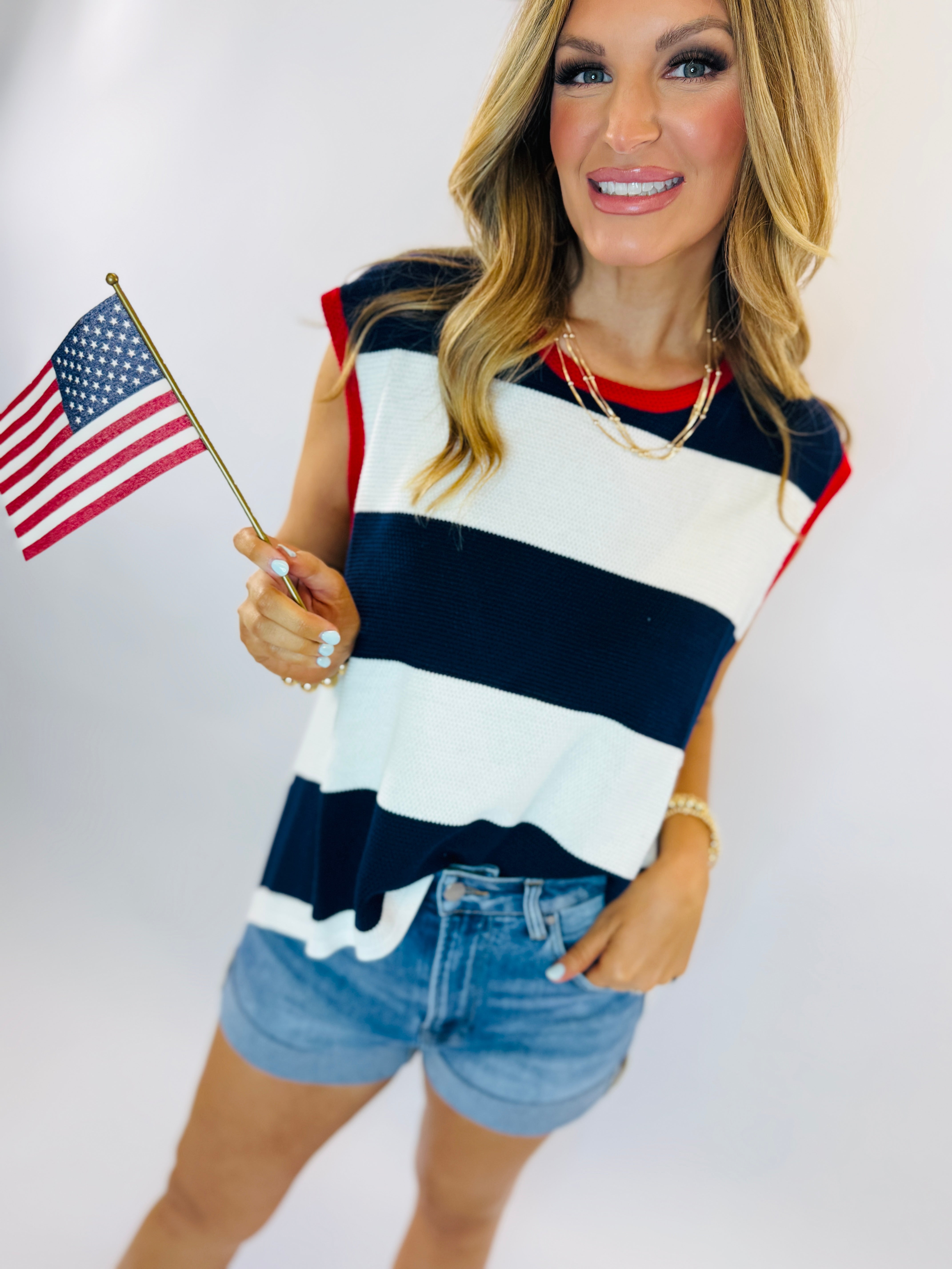 Woman wearing navy and white striped tank top with red trim, holding small American flag