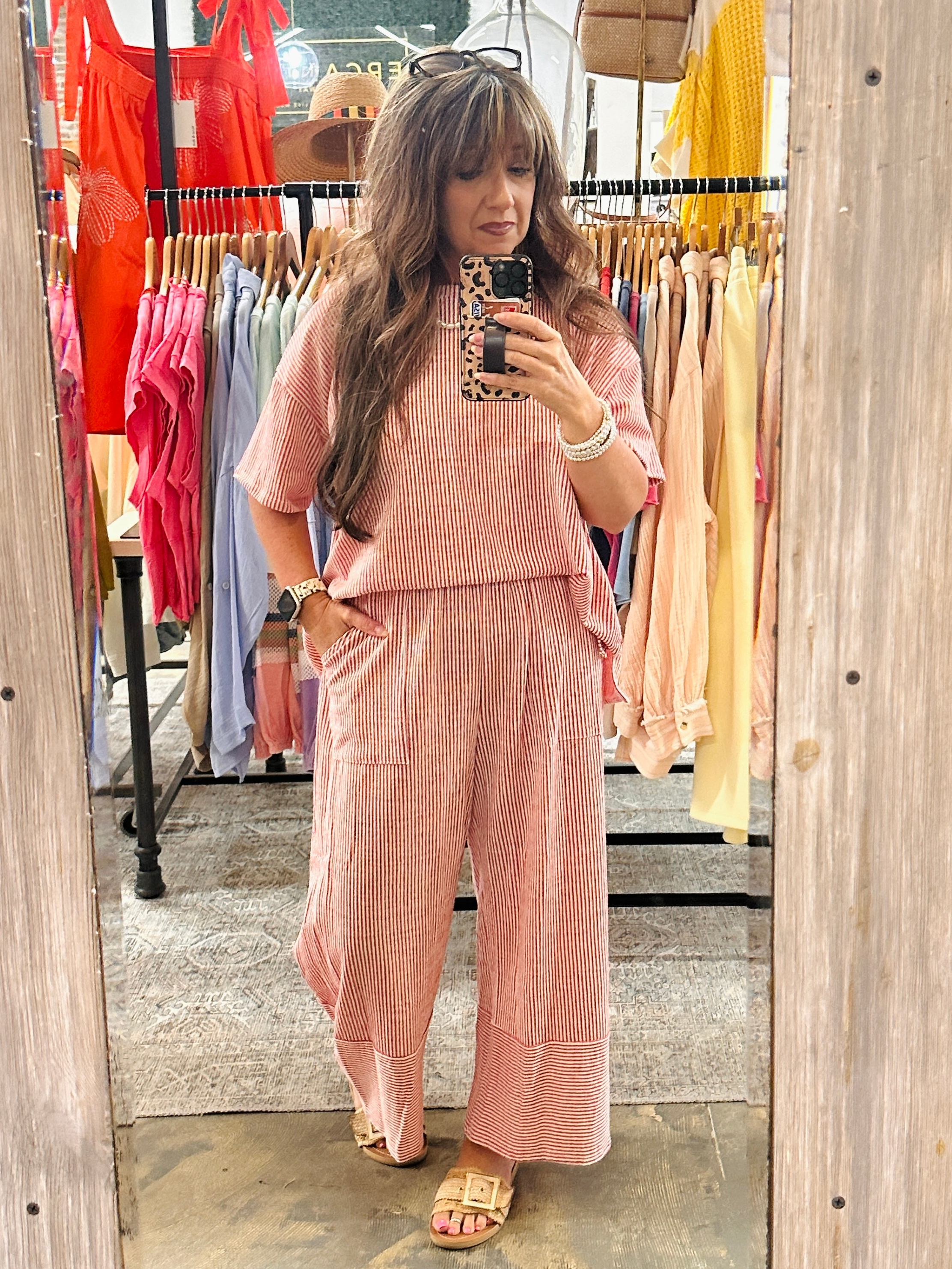 Woman wearing pink and white striped two-piece set with short sleeve top and wide-leg pants in clothing store dressing room.