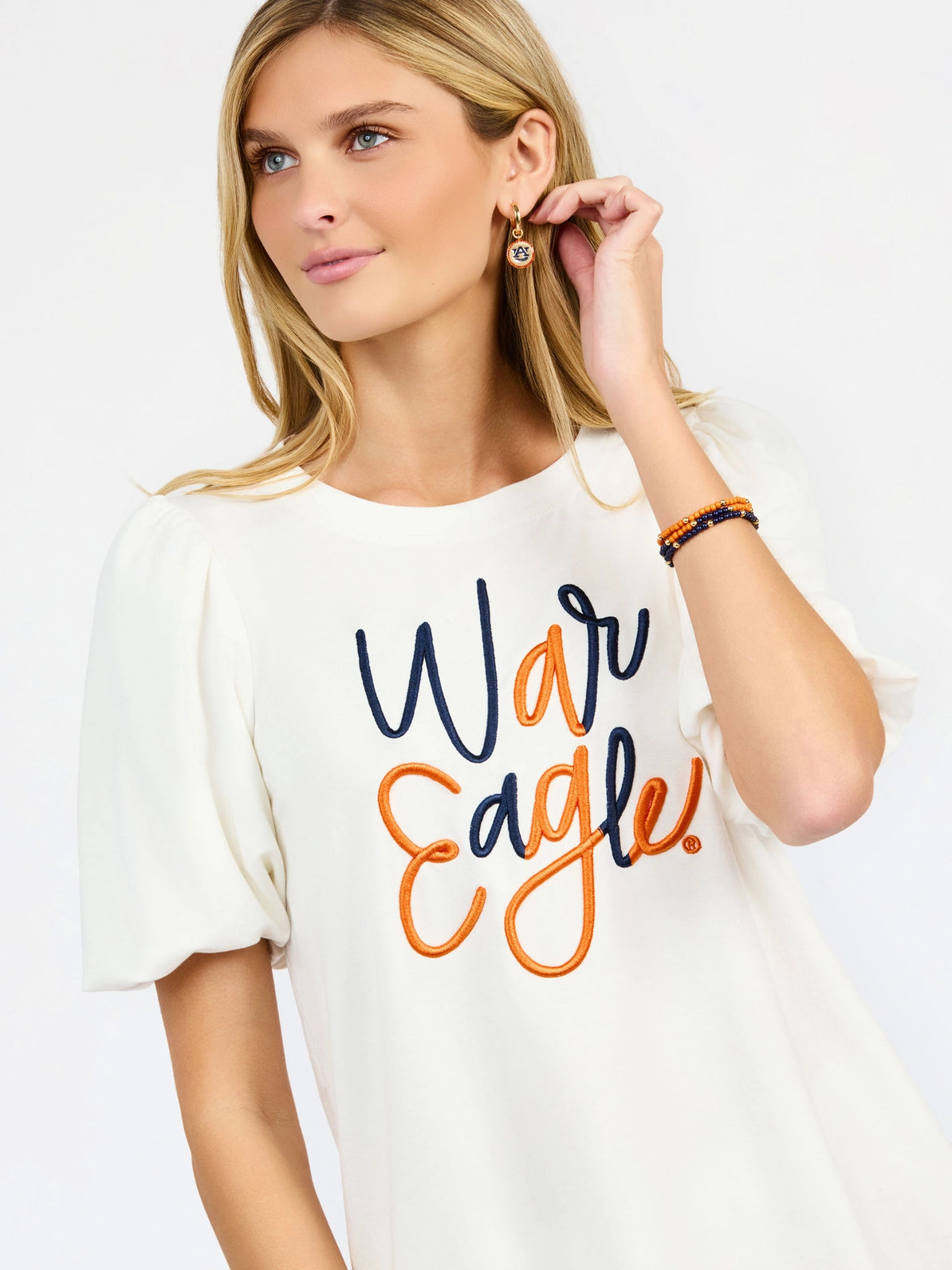 White short-sleeve top with embroidered navy and orange "War Eagle" script lettering, styled with Auburn University earrings.