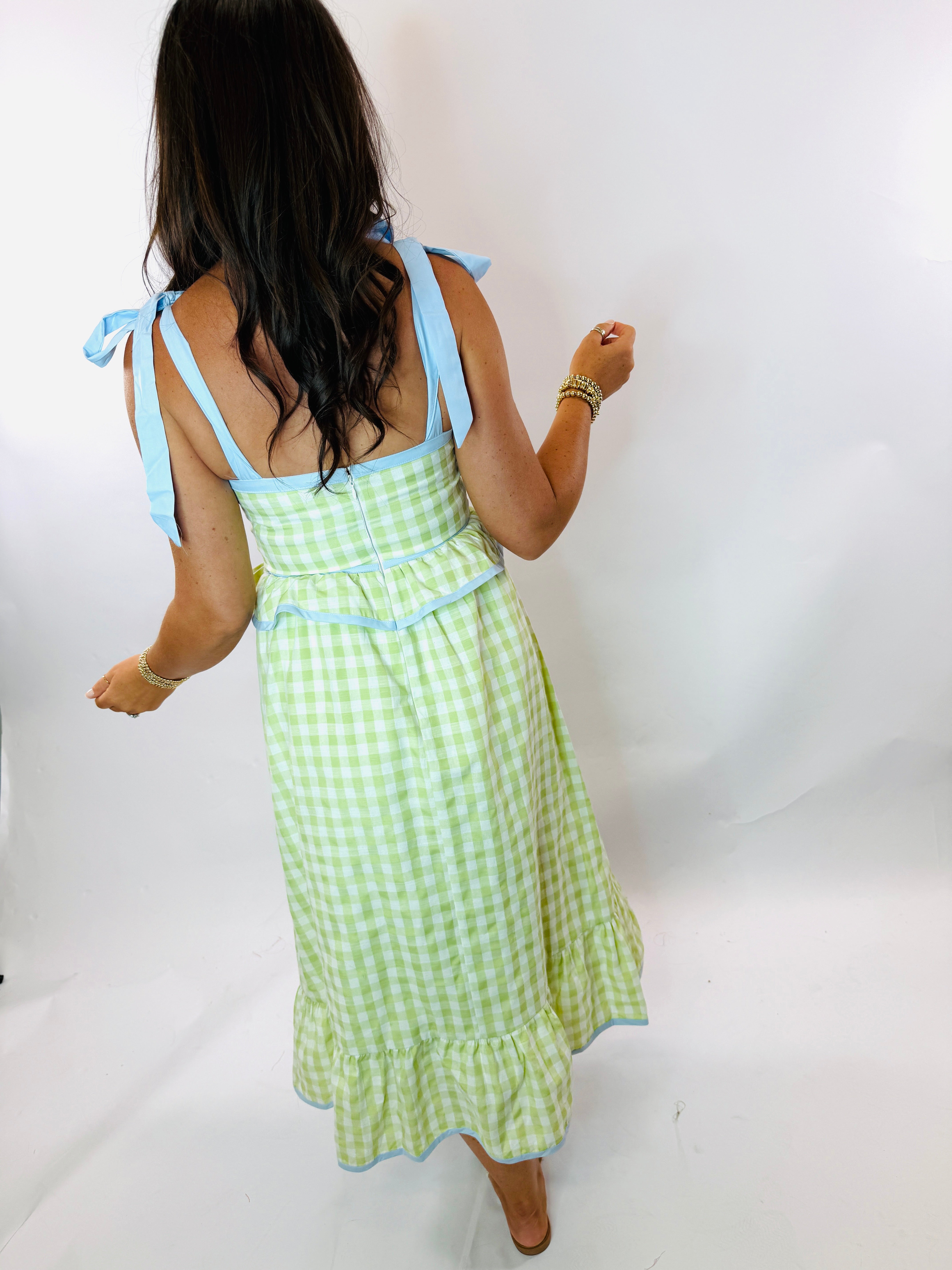 Woman wearing green and white gingham midi dress with blue ribbon shoulder ties and tiered ruffle hem