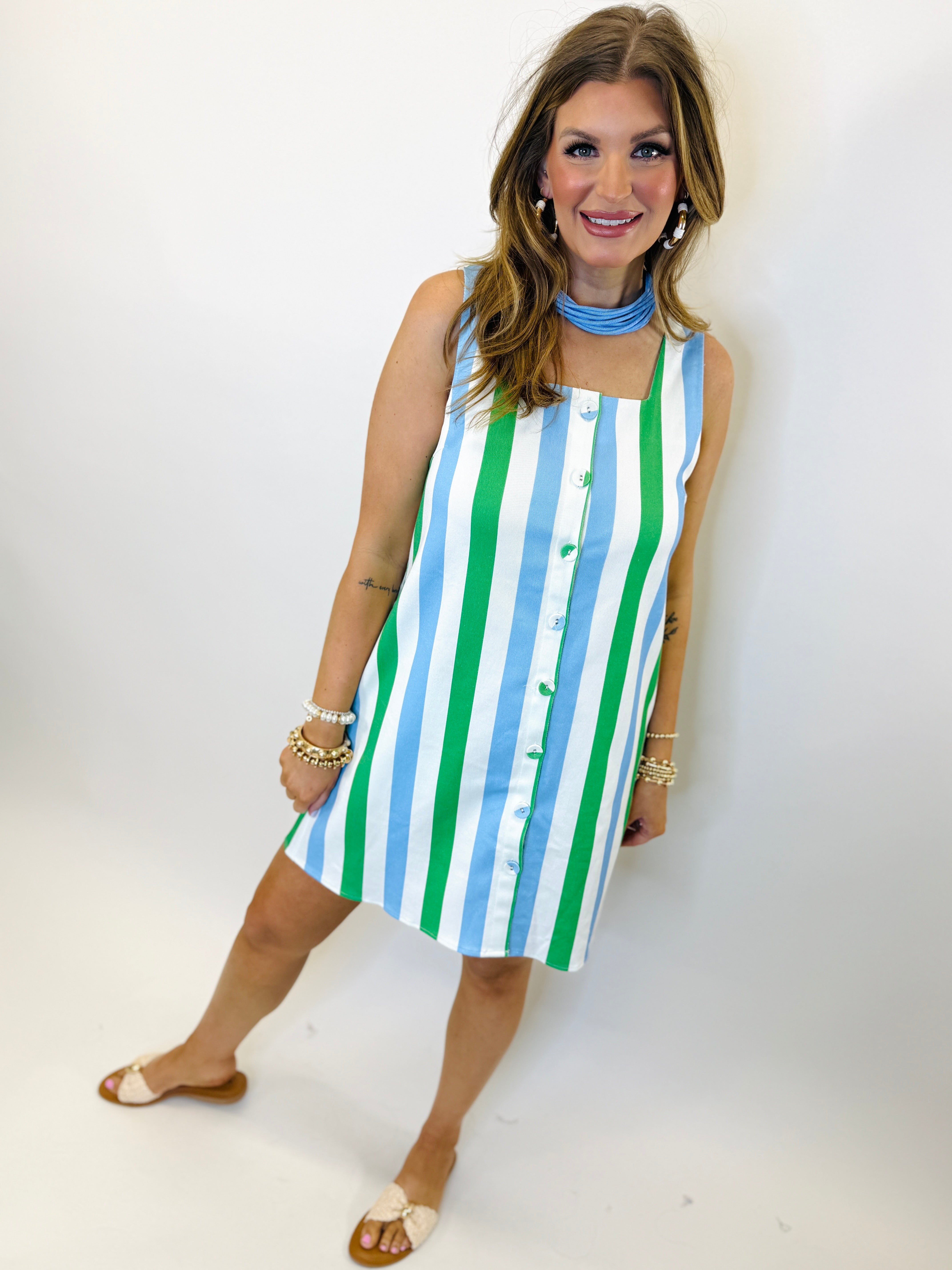 Woman wearing blue and green striped sleeveless button-front dress with matching choker necklace and gold jewelry.