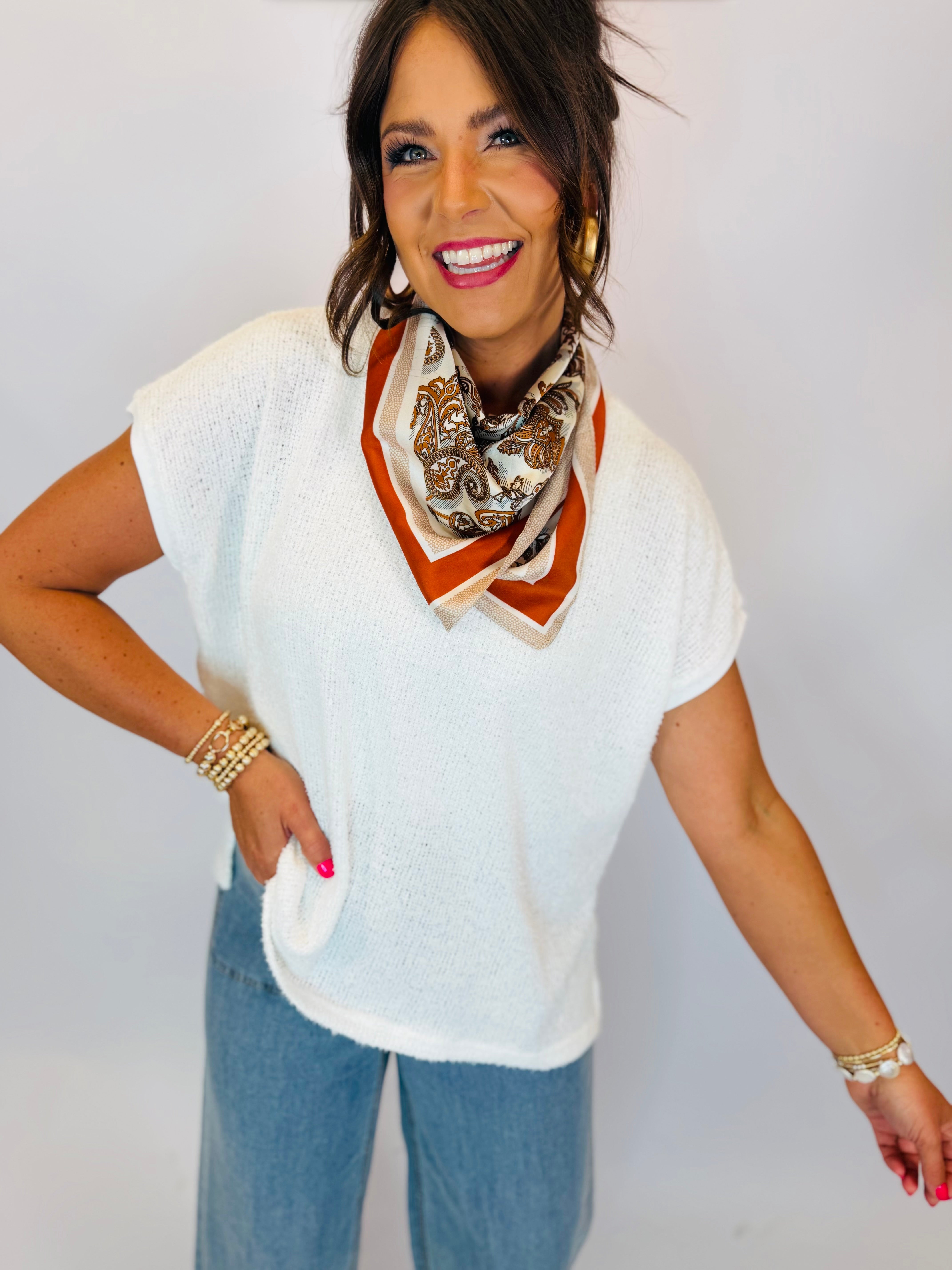 White short-sleeve knit sweater top styled with a paisley neck scarf and light wash jeans.